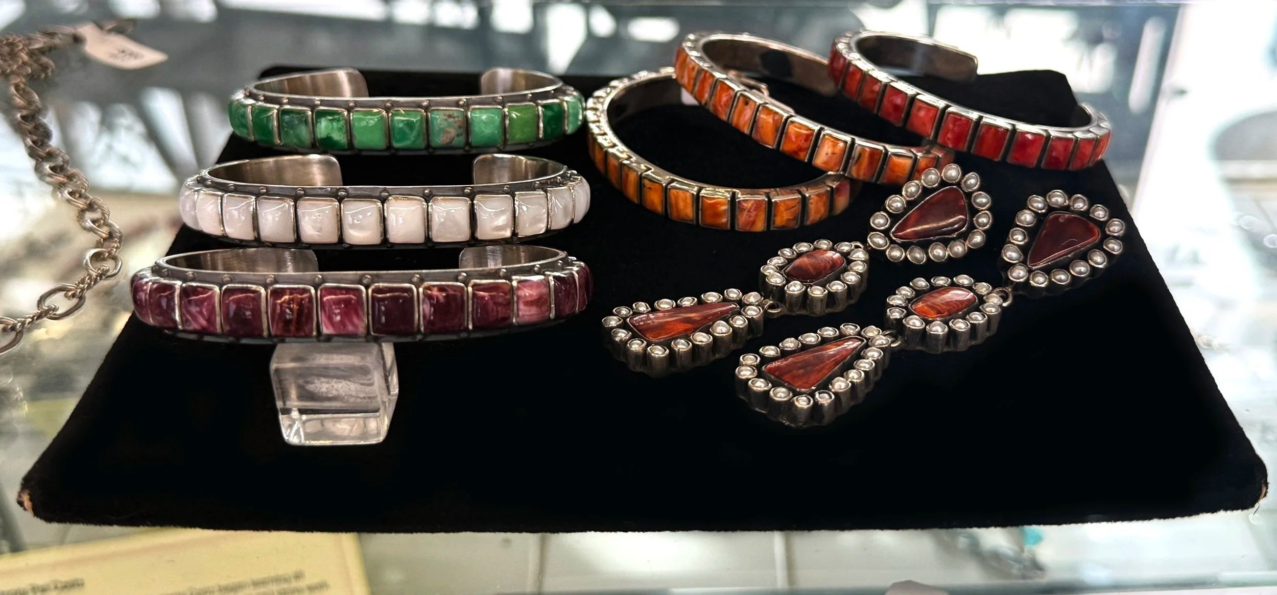 Collection of colorful jewelry including turquoise, coral, white, and red bangles, along with matching earrings, displayed on a black surface.
