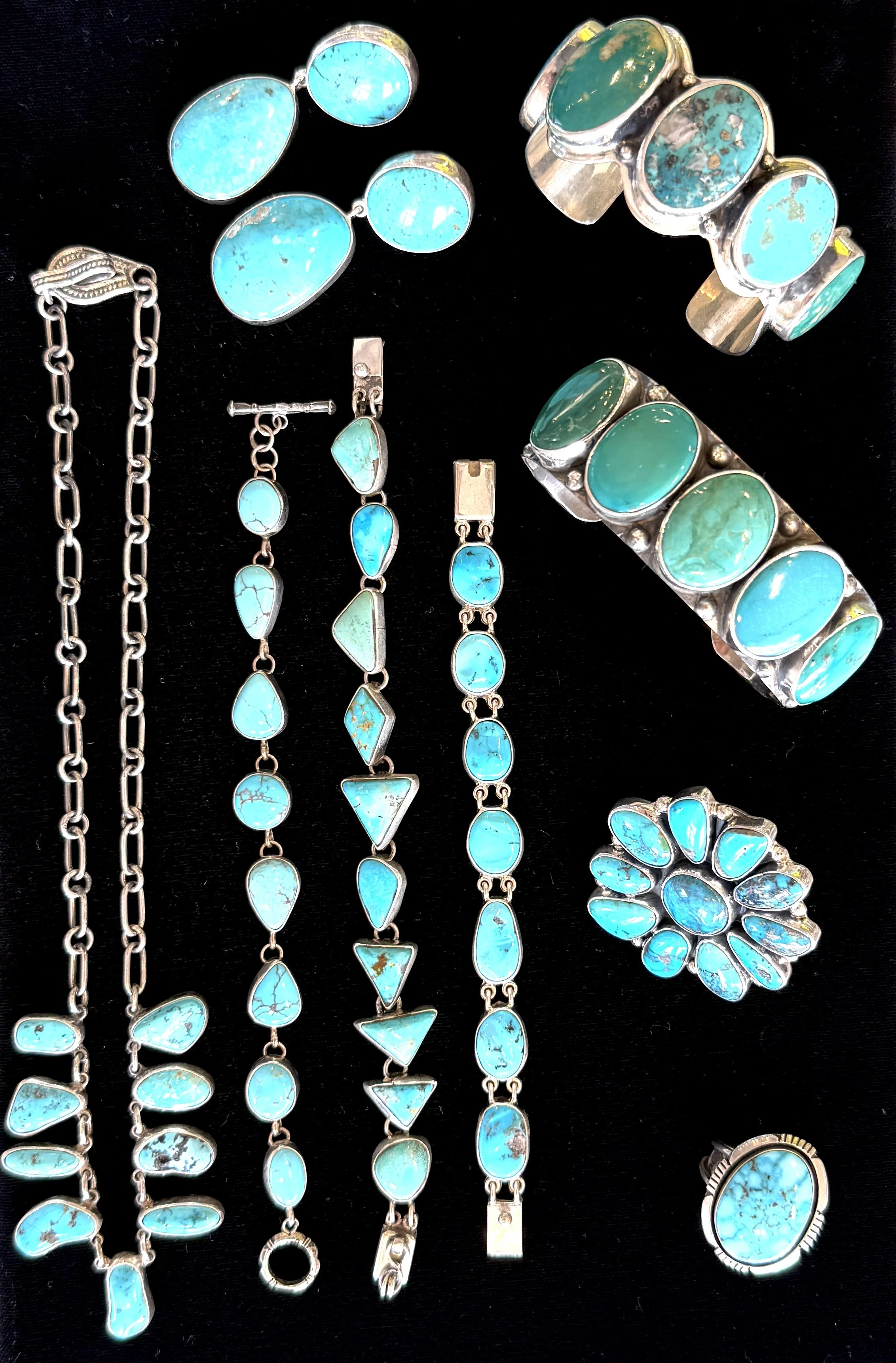 Collection of turquoise jewelry including rings, bracelets, necklaces, and earrings arranged on a black surface.