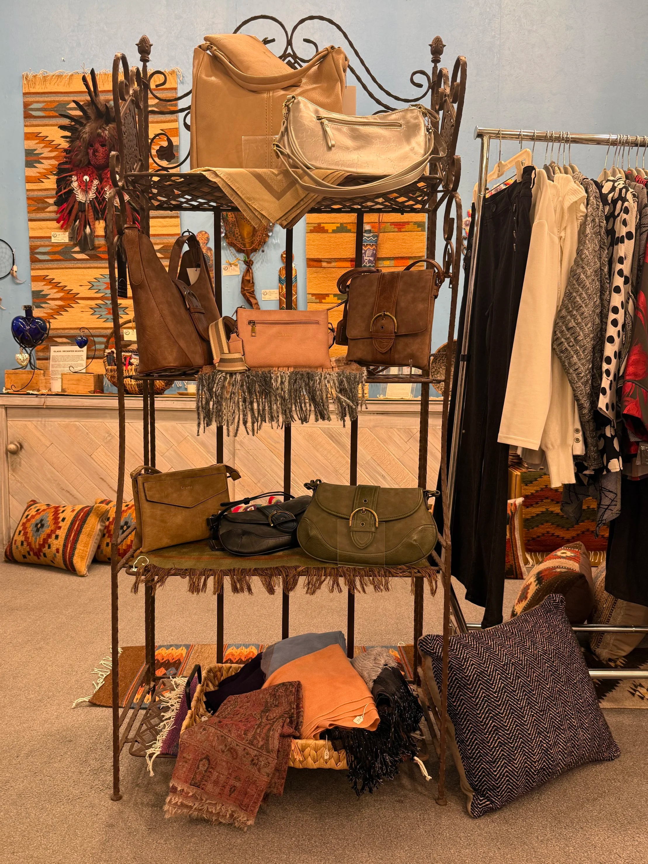 Display of handbags, scarves, pillows, and clothing in a boutique clothing, art, and gift store.