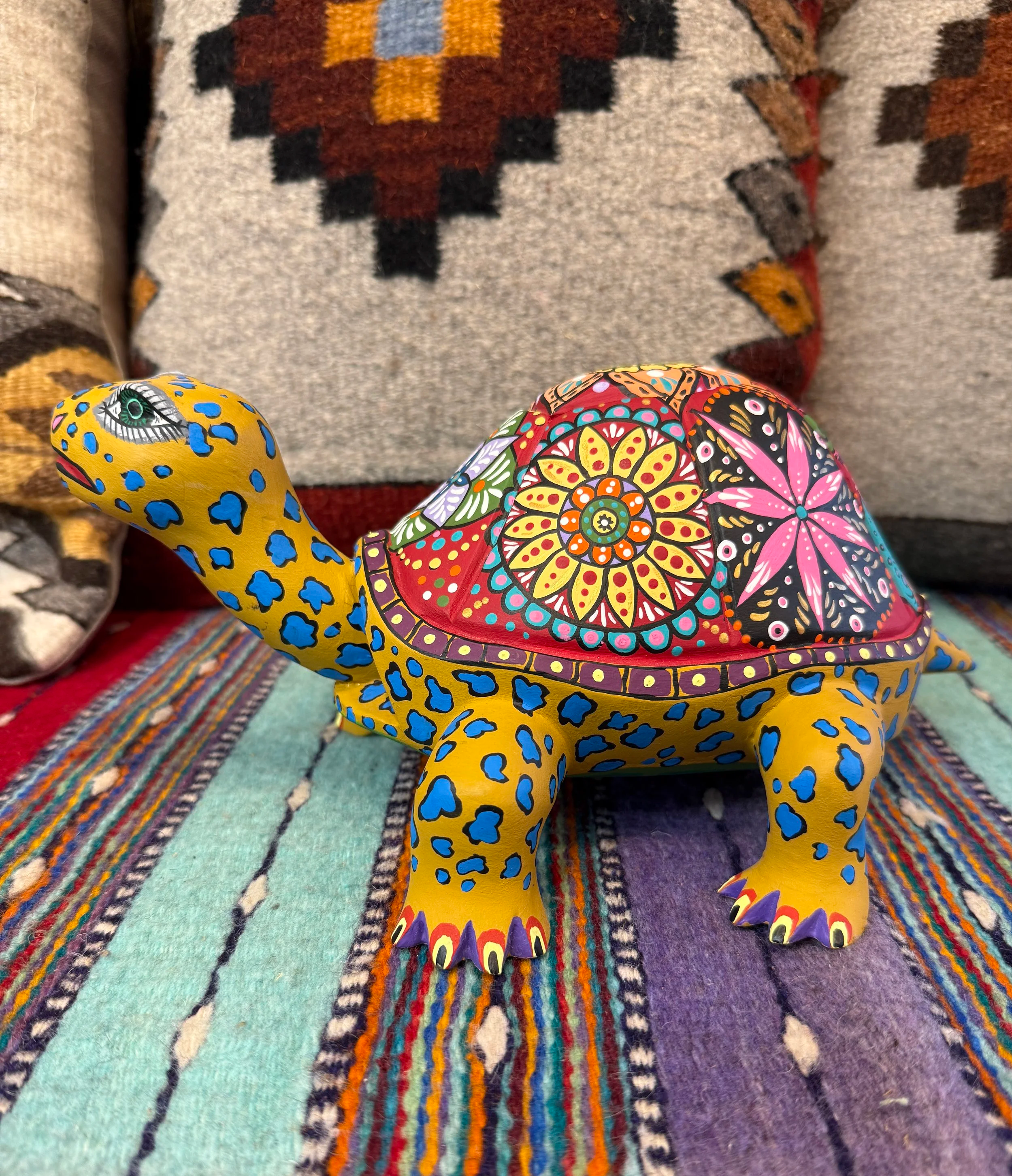 A colorful decorative turtle sculpture with intricate floral and geometric designs on its shell, placed on a multicolored striped mat.