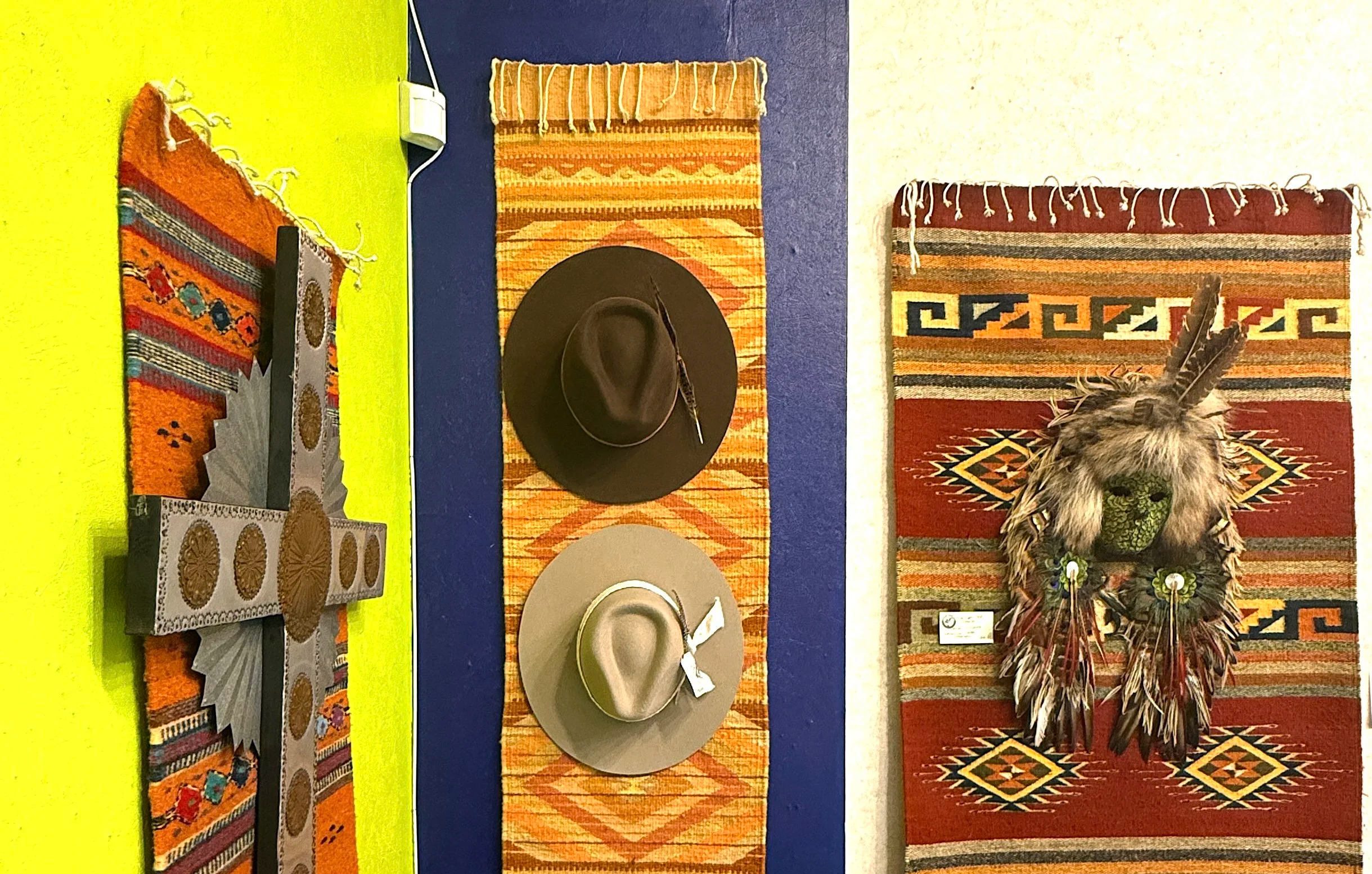 Display of woven rugs, hats, and clothing in a clothing and art store with colorful walls and a clothing rack.
