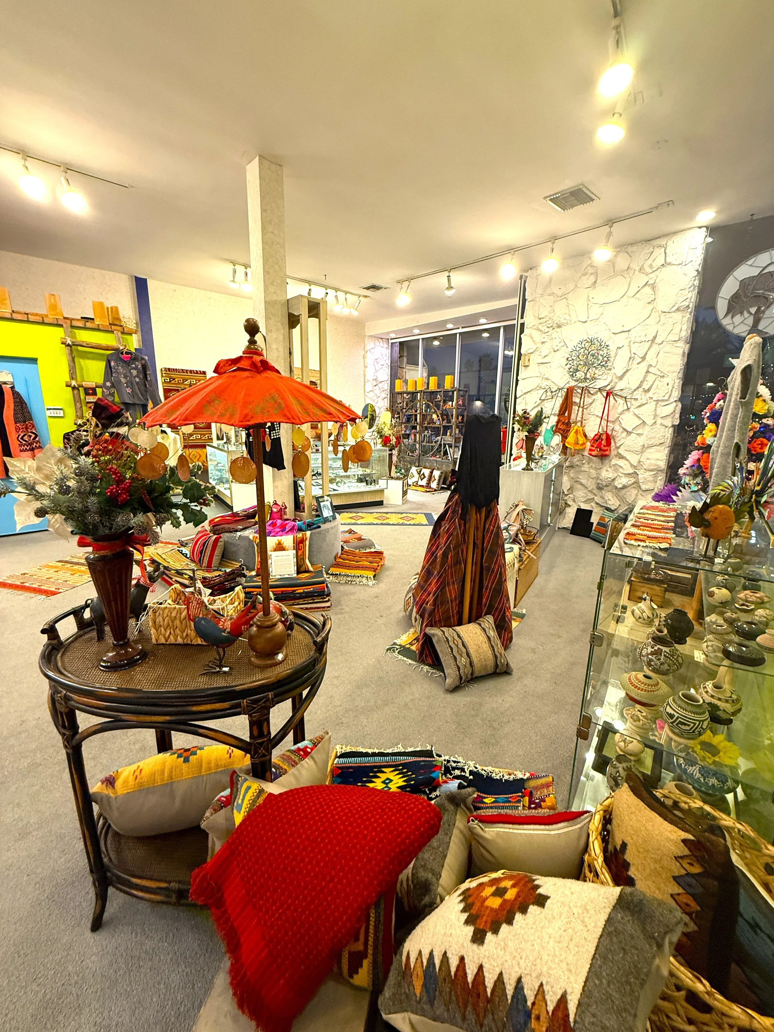 The interior of a gift shop and gallery decorated with various handmade crafts, colorful textiles, pottery, and accessories.