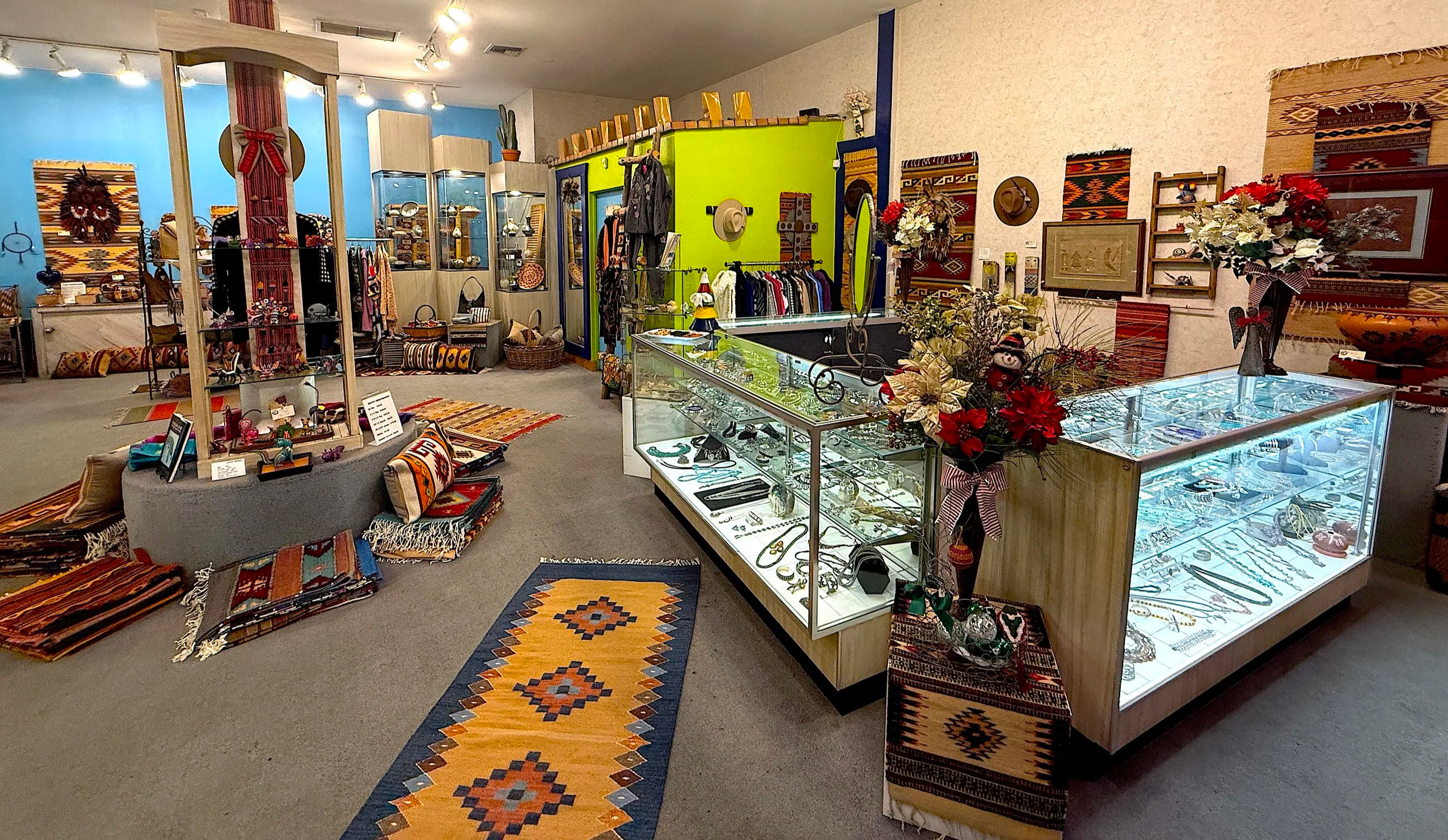 Interior of a Moon Dancer in the South Bay displaying jewelry, textiles, and decorative art pieces, with glass display cases, colorful rugs, and woven wall hangings.