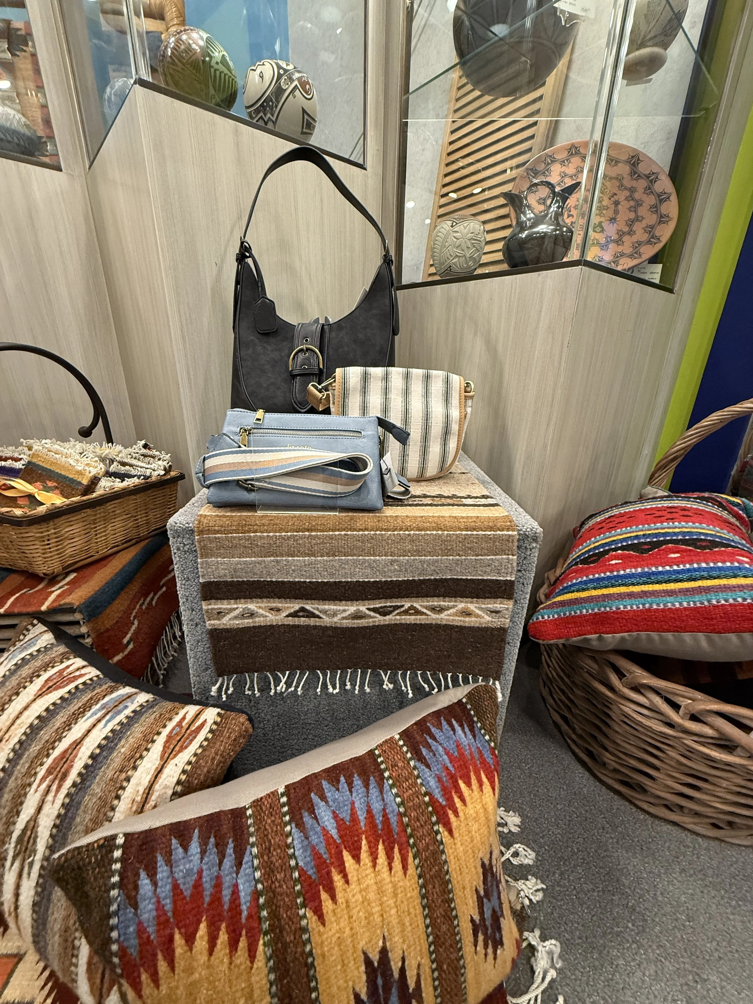 A display of handmade decorative bags and woven pillows with unique pottery behind.