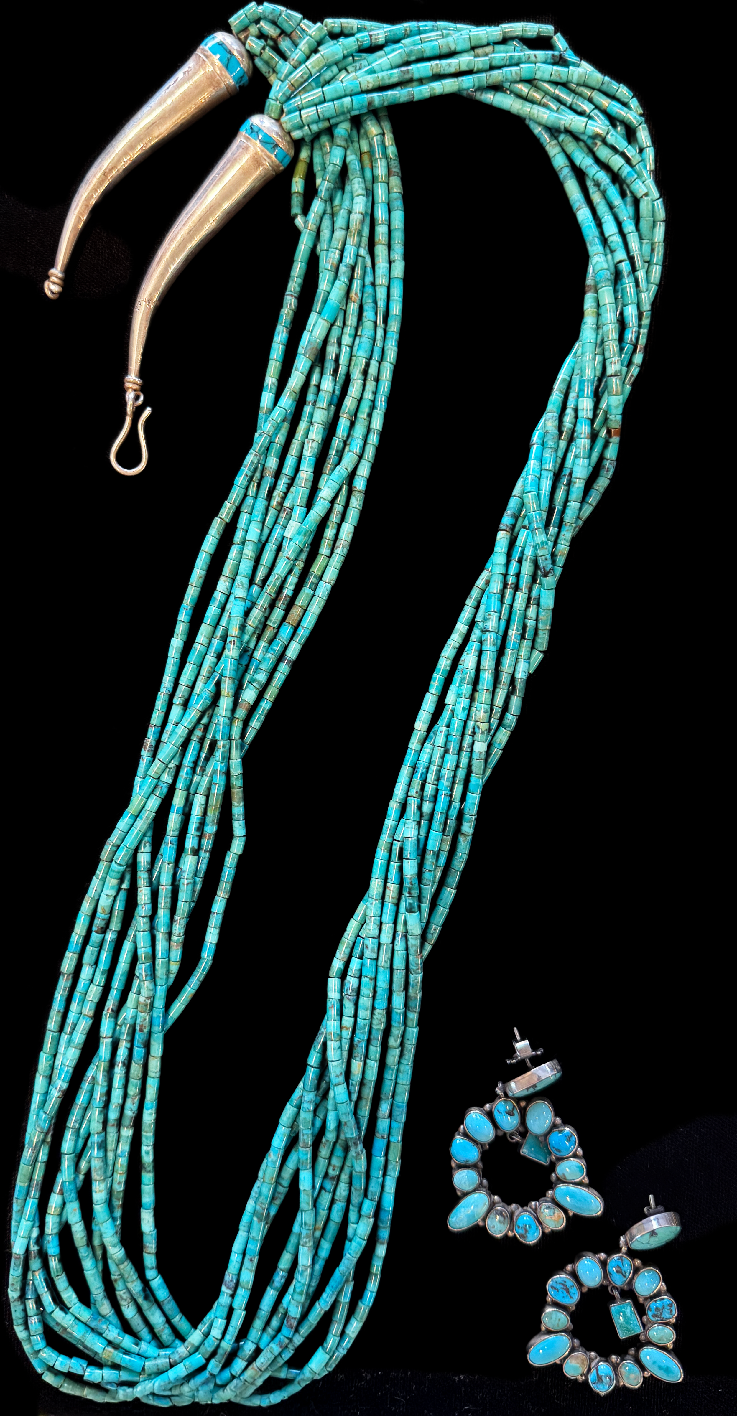 Turquoise jewelry set displayed on black fabric, including a long layered turquoise necklace with silver hooks and matching turquoise earrings with silver settings, on a jewelry display table.
