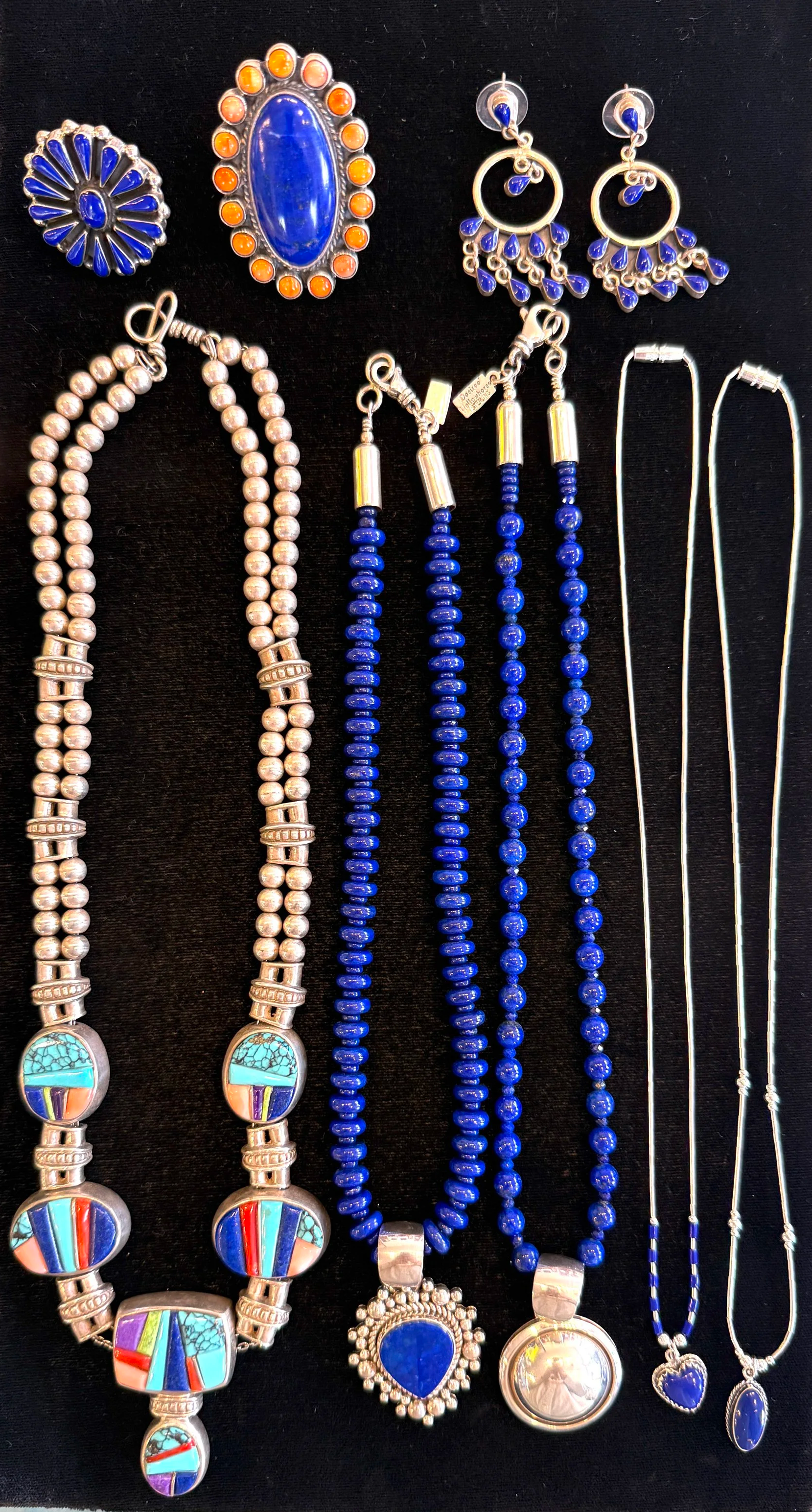 Collection of jewelry including rings, earrings, necklaces, and chains with blue and silver designs displayed on black fabric.