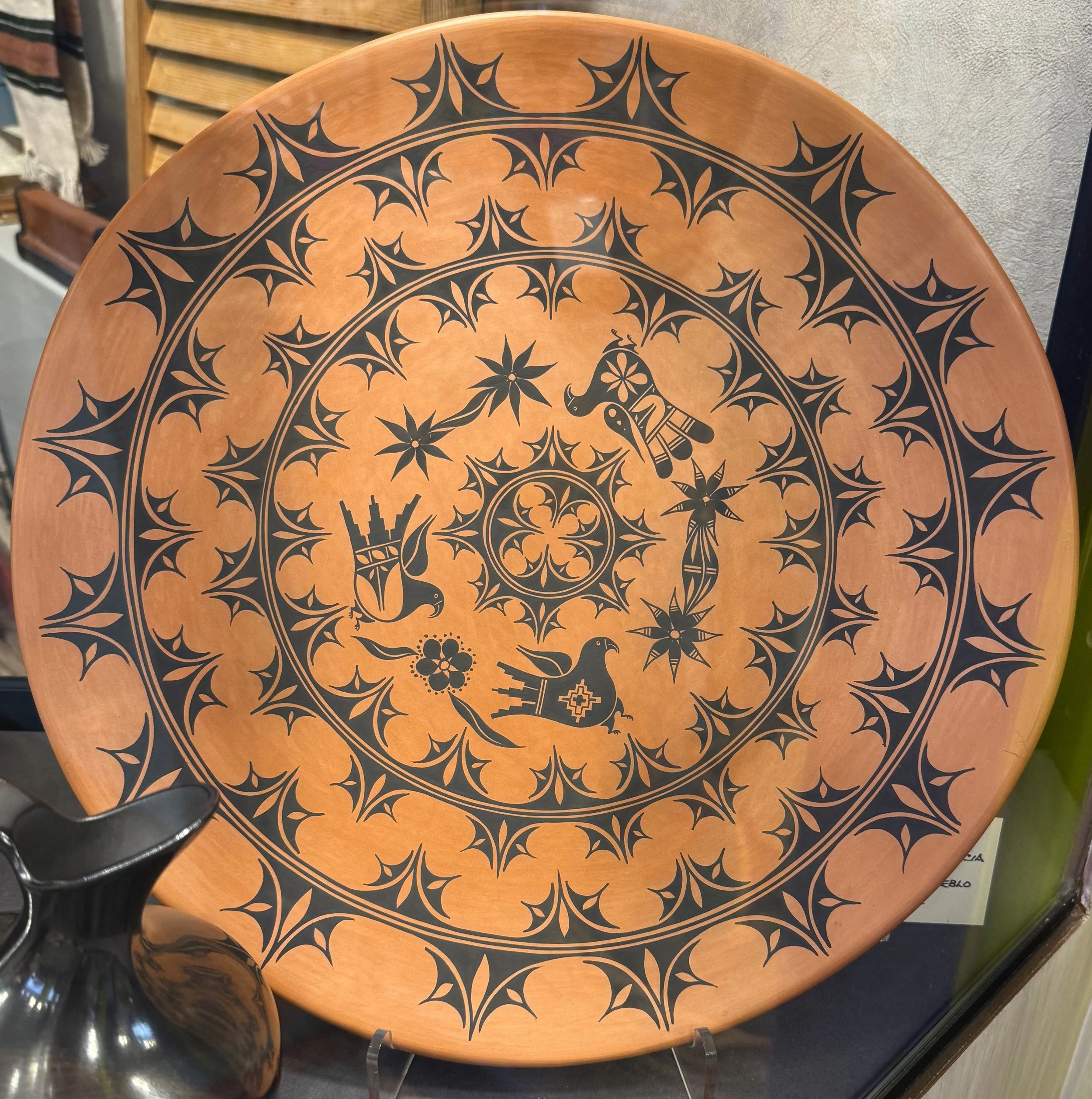 Round ceramic decorative plate with black geometric and nature-inspired patterns, including birds, flowers, and abstract shapes.