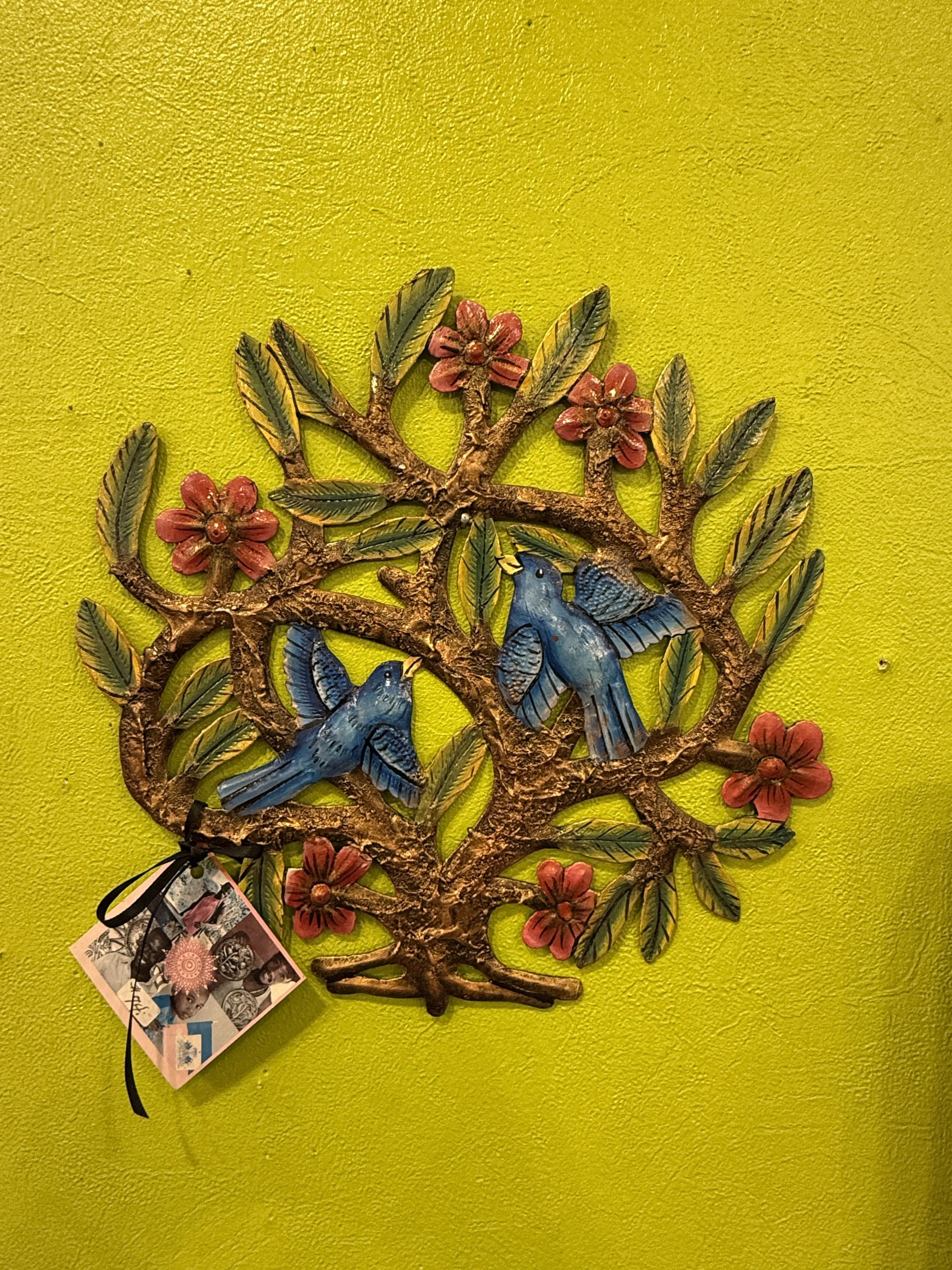 Decorative Native-American wall hanging with two blue hummingbirds, pink flowers, and green leaves on a yellow wall.