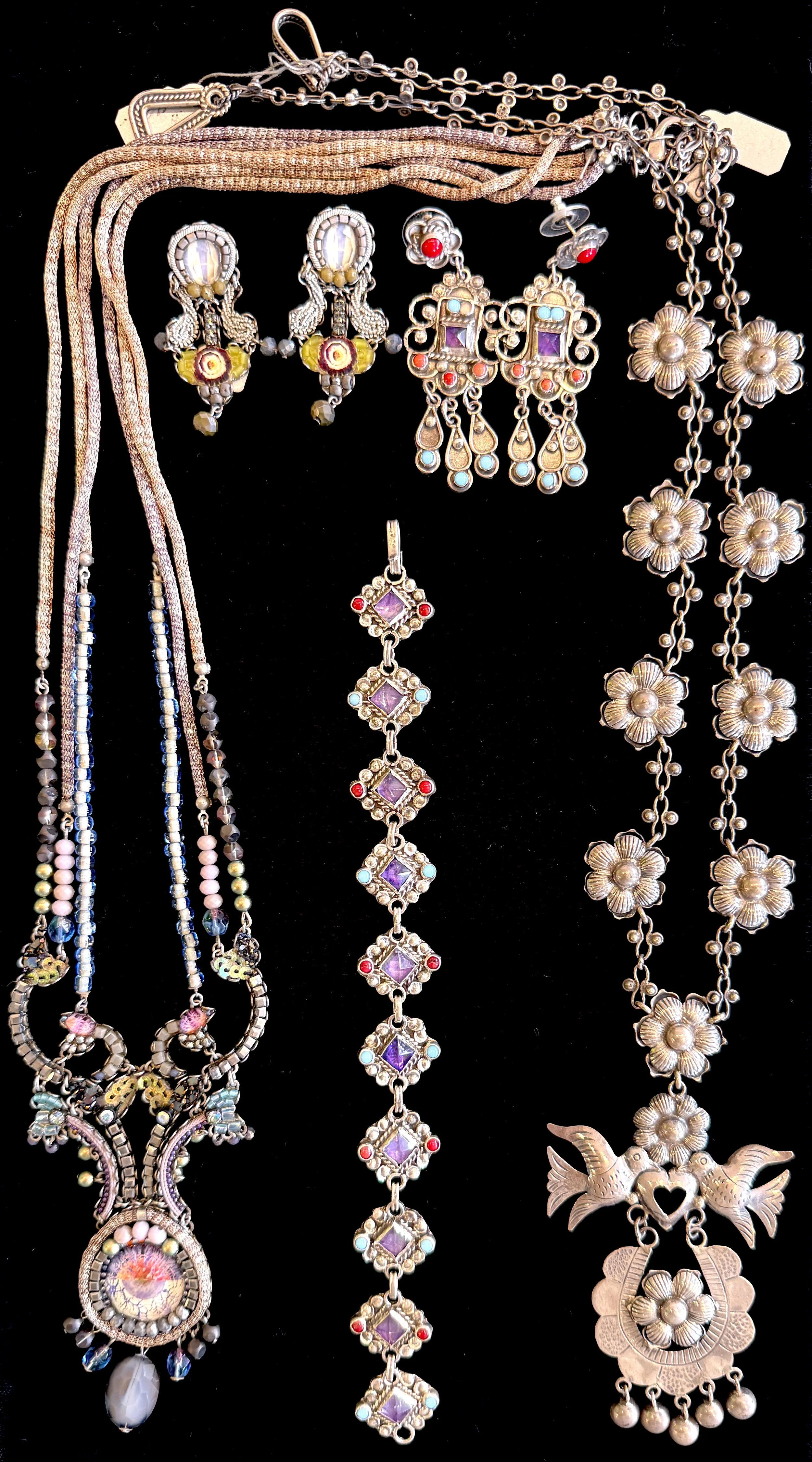 Collection of various silver jewelry pieces including necklaces, earrings, and bracelets with colorful stones and floral designs displayed against a black background.