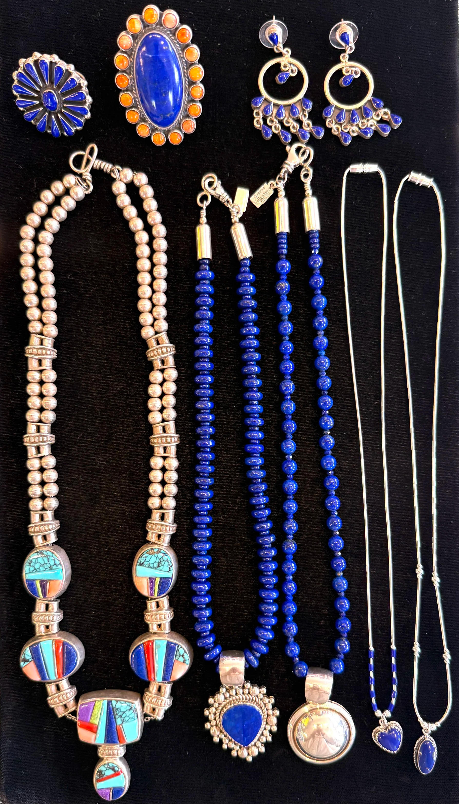 Assorted jewelry including earrings, necklaces, and pins with blue and turquoise stones on a black background.