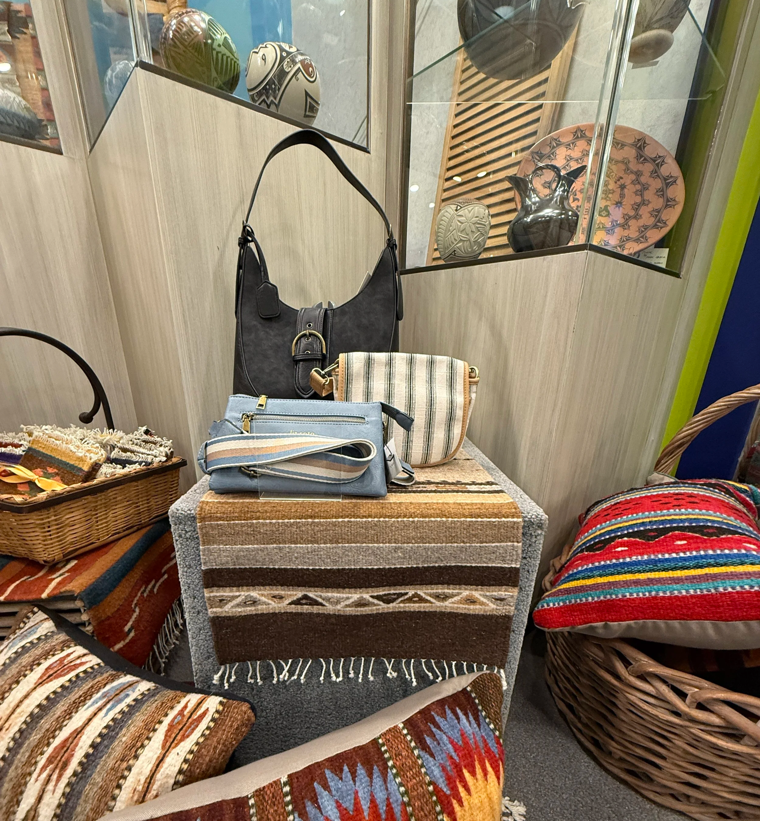 Display of handbags and accessories on a small table in a boutique store with decorative pottery and textiles in the background.