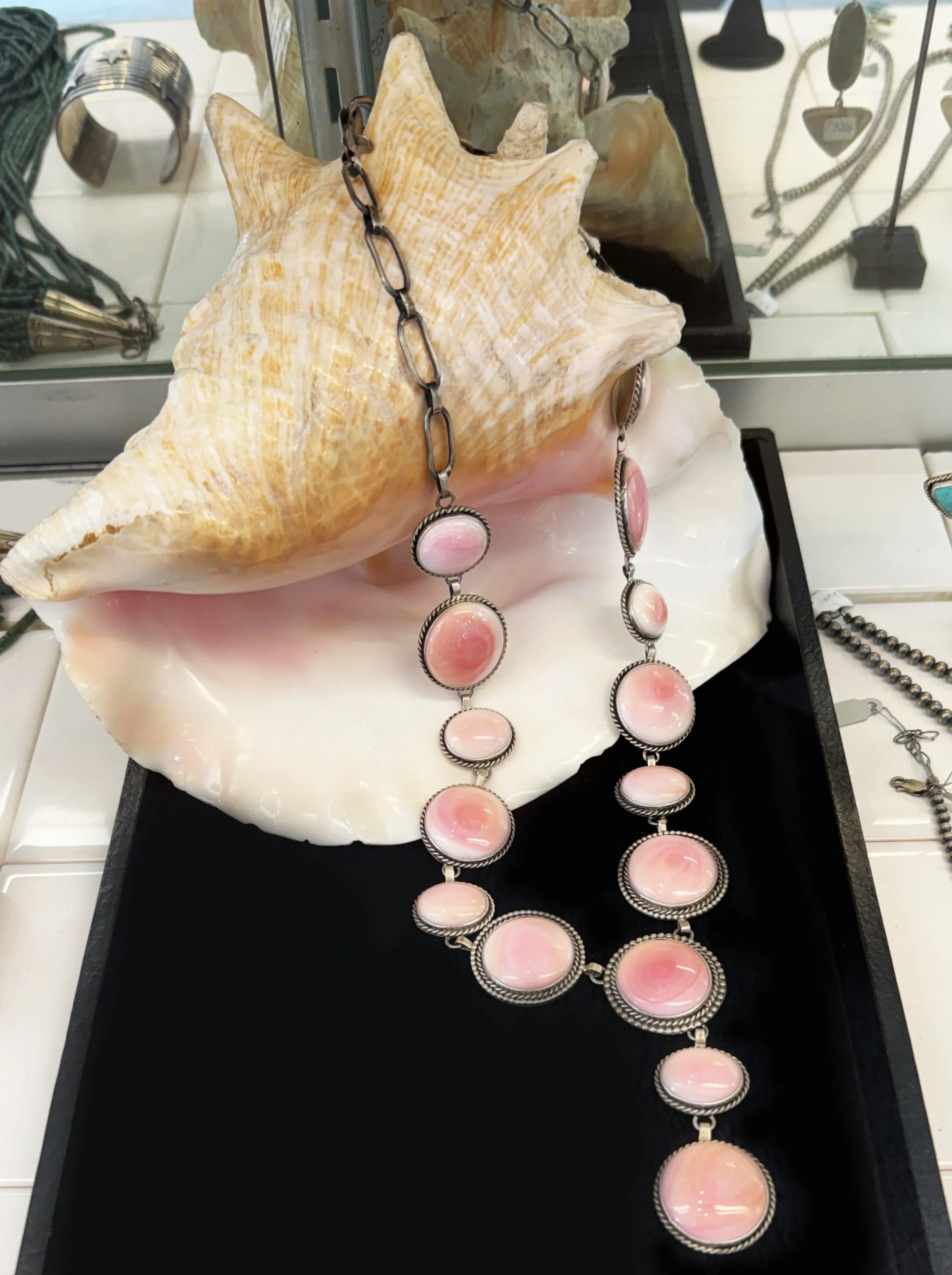 Pink and silver necklace and matching earrings displayed on a seashell within a jewelry display case.