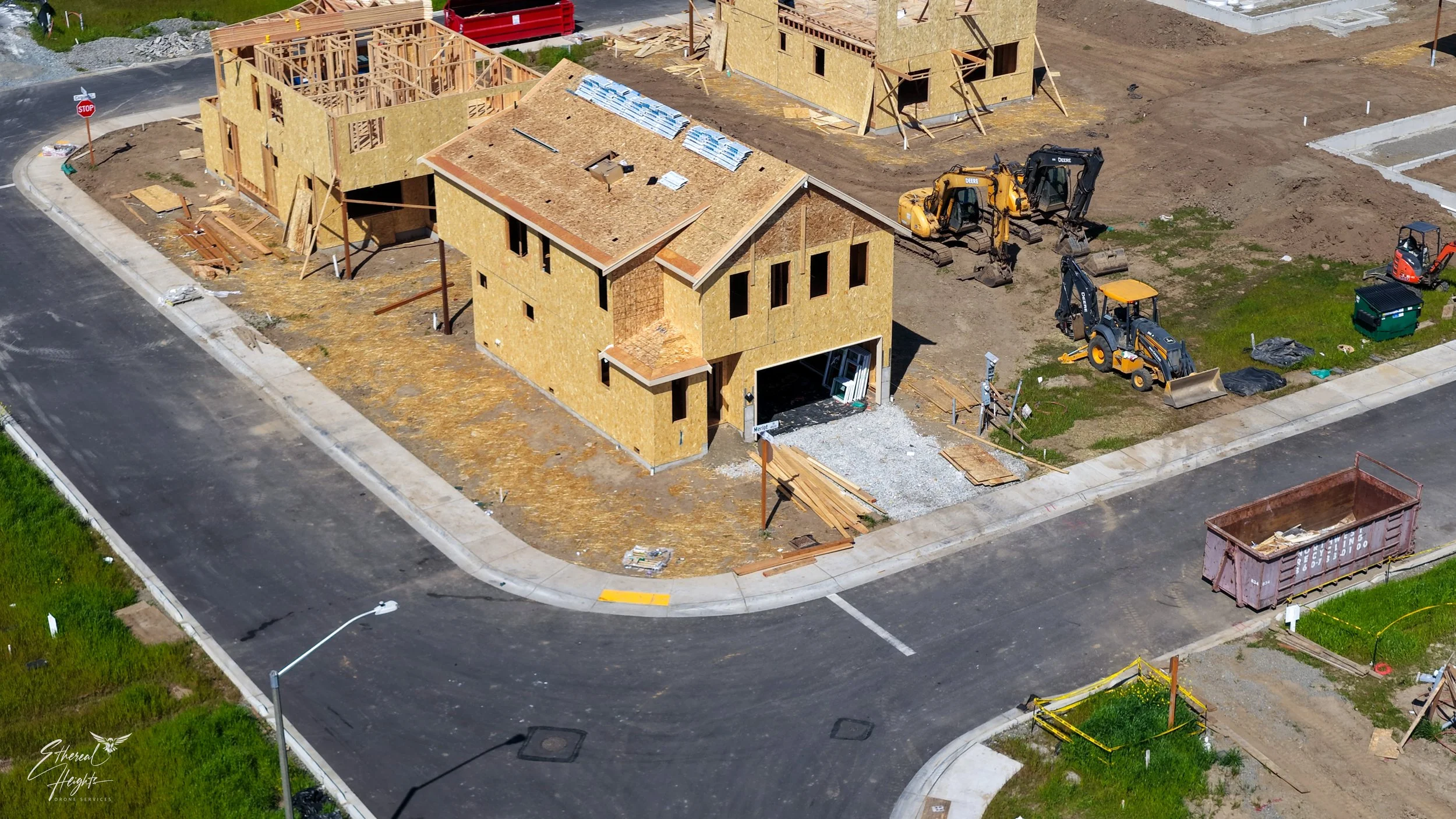 Aerial view of a construction site with houses under building, surrounded by roads, with construction equipment and building materials.