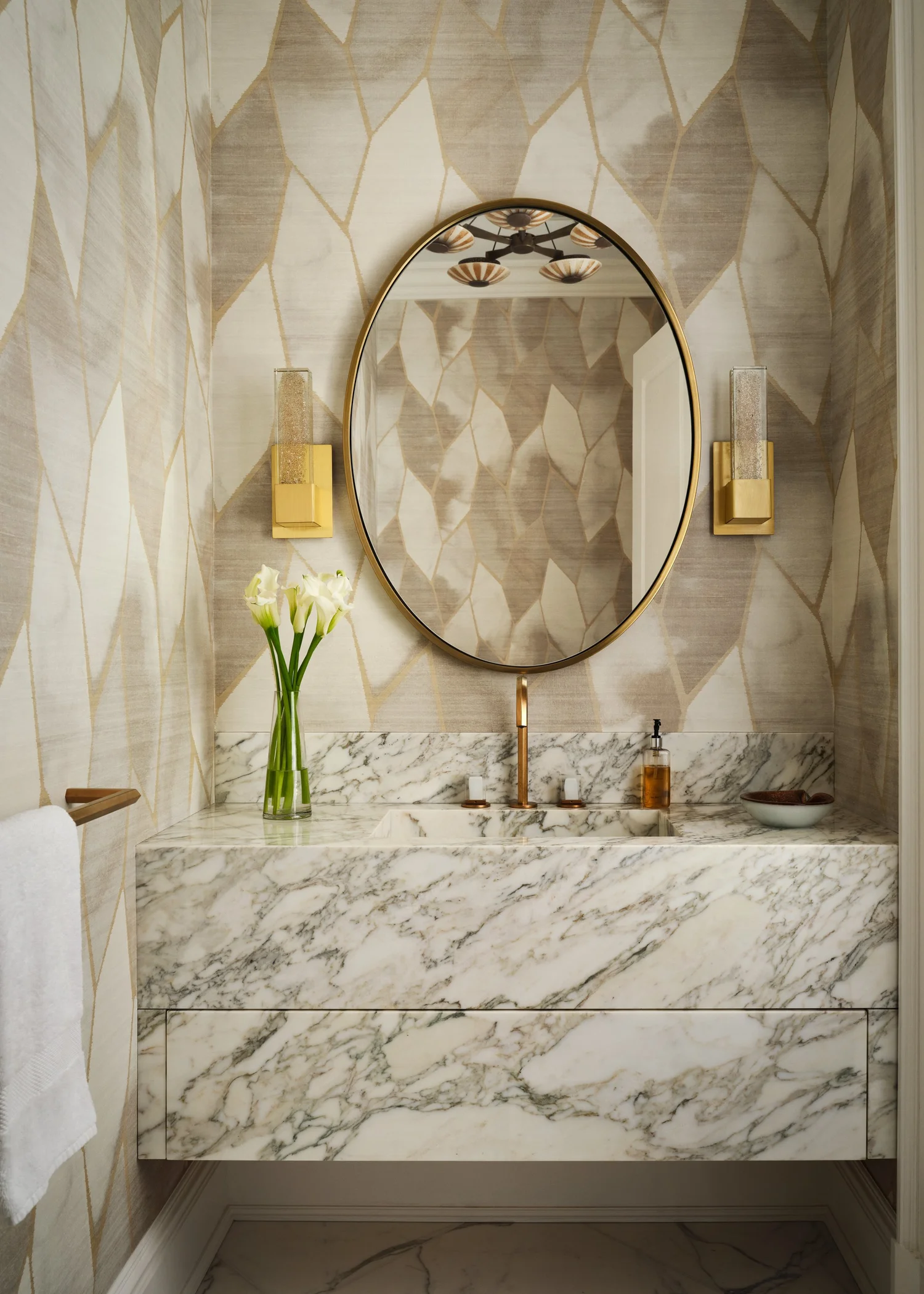 A custom powder room with book-matched marble, a round mirror, and brass fittings, detailing by Michele Bitter Designs