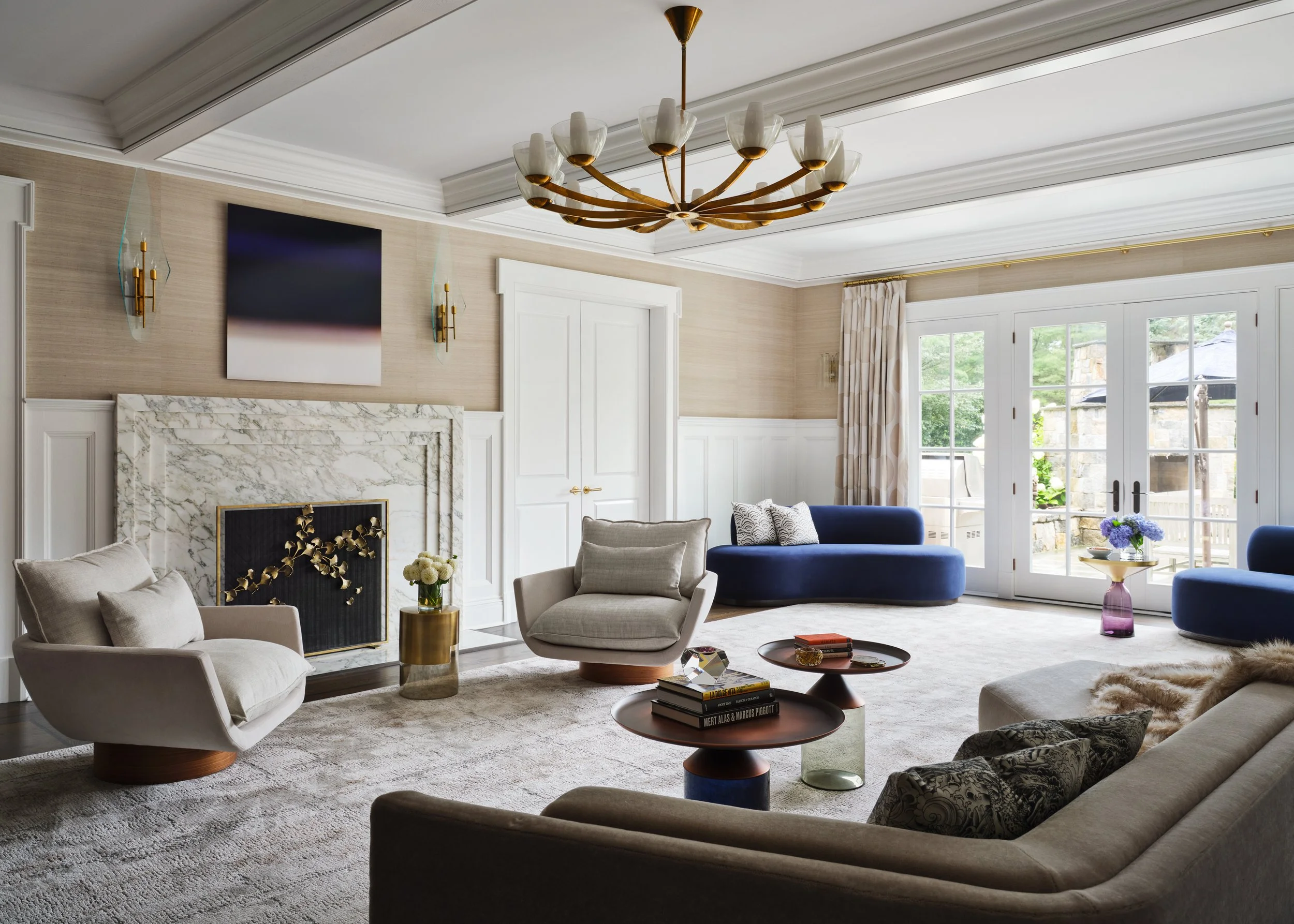 A light-filled living room with a curved sofa and marble fireplace in a Greenwich, Connecticut home designed by Michele Bitter Designs