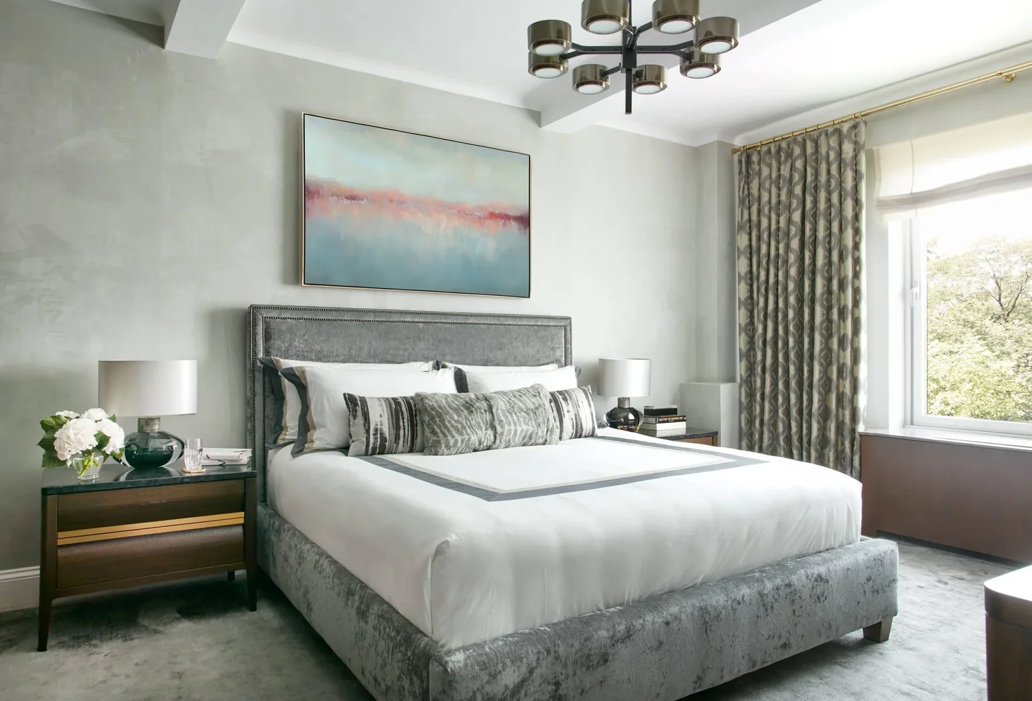 A serene primary bedroom with an upholstered bed, layered textiles, and soft natural light in a Fifth Avenue apartment designed by Michele Bitter Designs