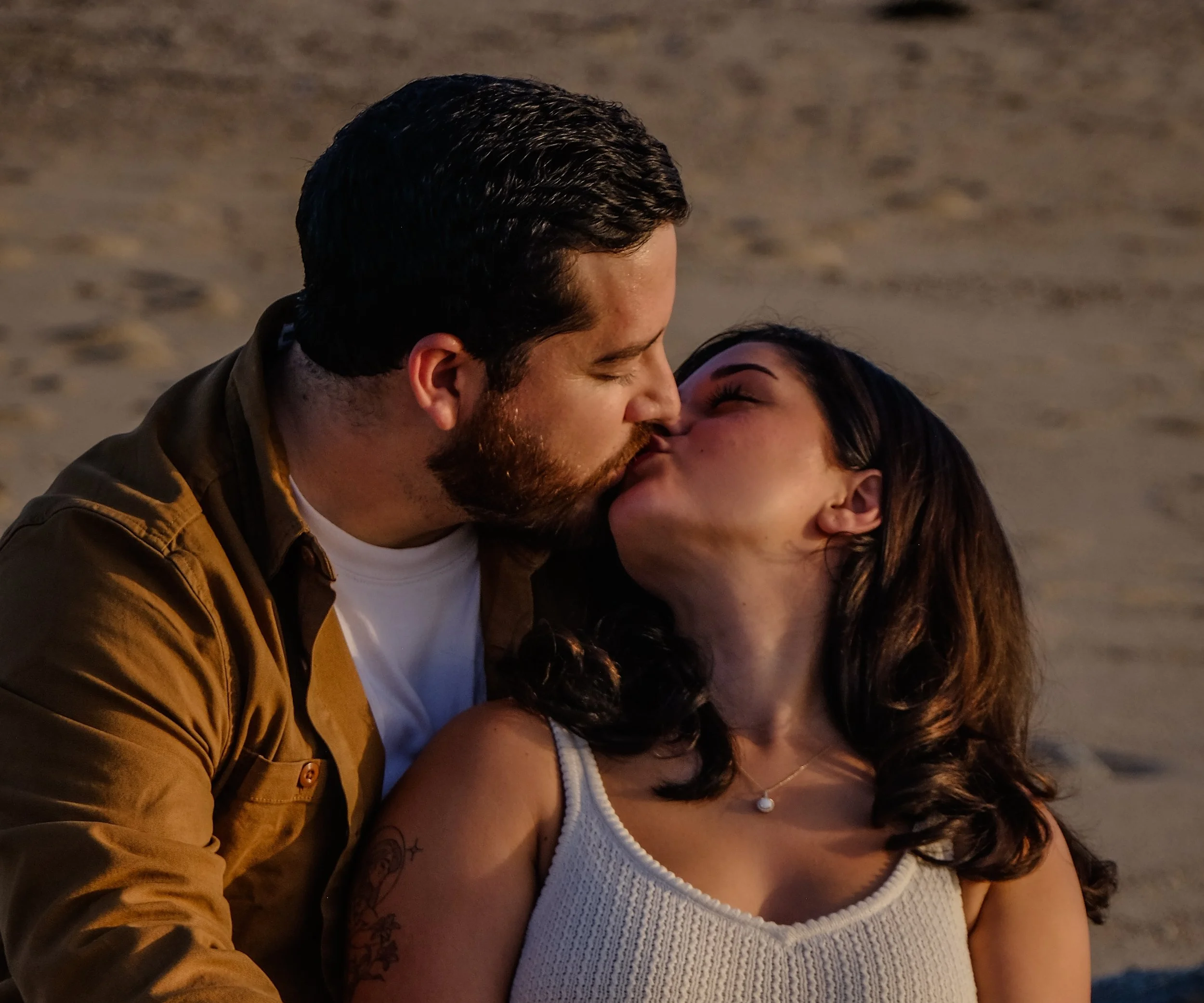 A man and woman sharing a kiss on a beach at sunset.