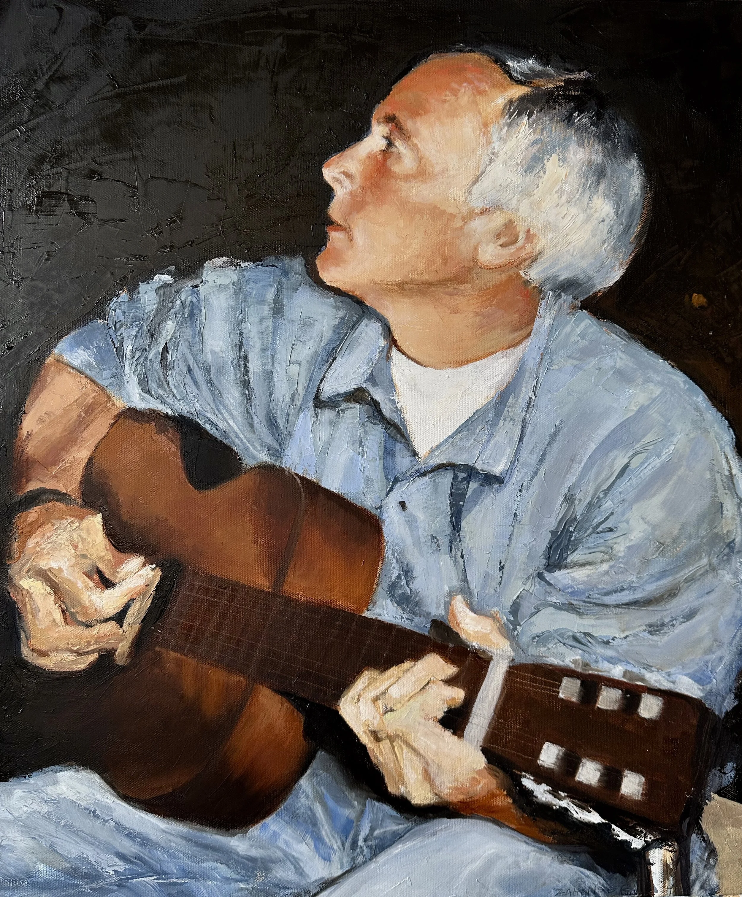 An older man with gray hair playing an acoustic guitar, looking upwards, wearing a light blue shirt against a dark background.