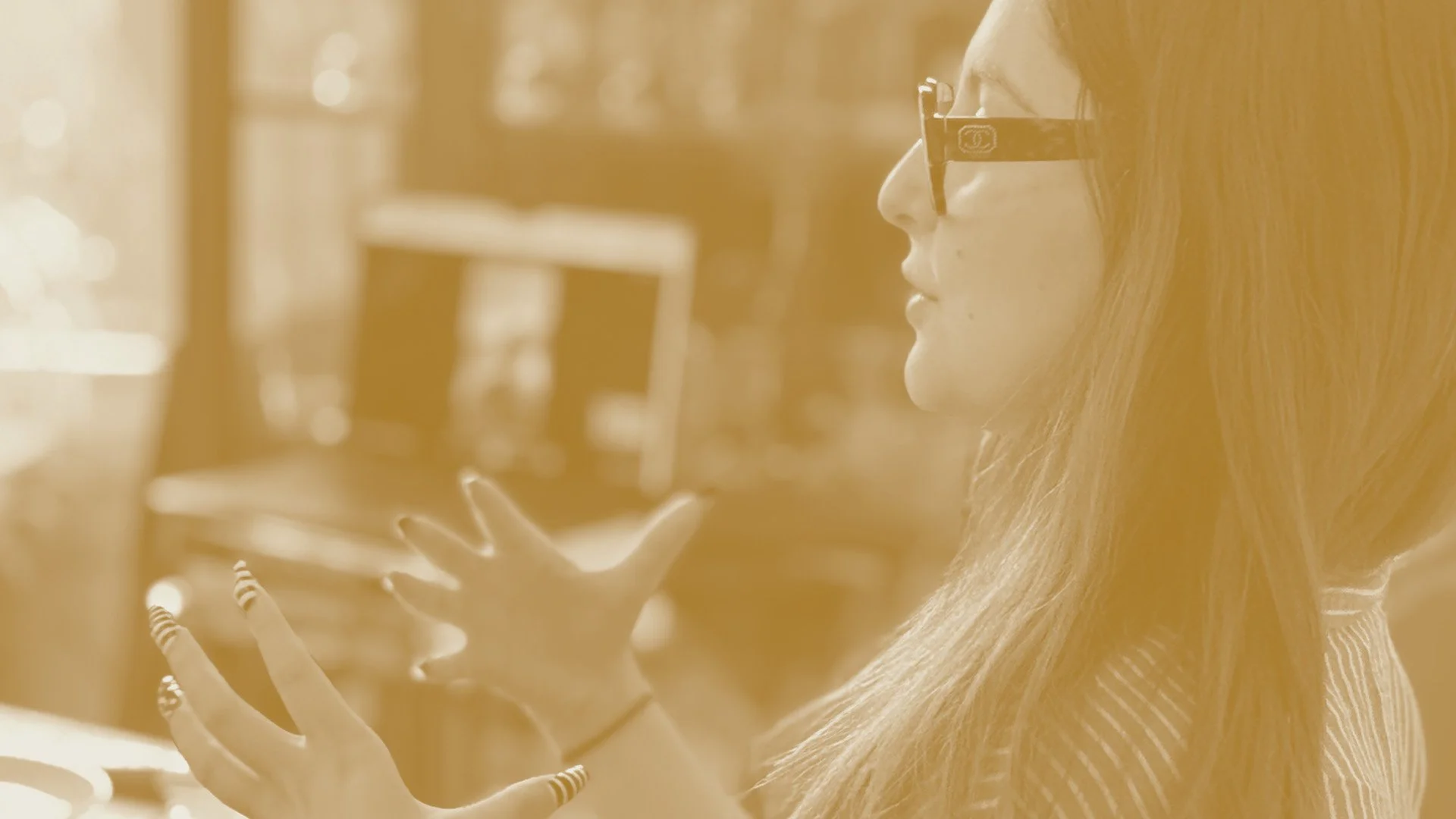 A woman with long hair and glasses in profile gesturing while speaking