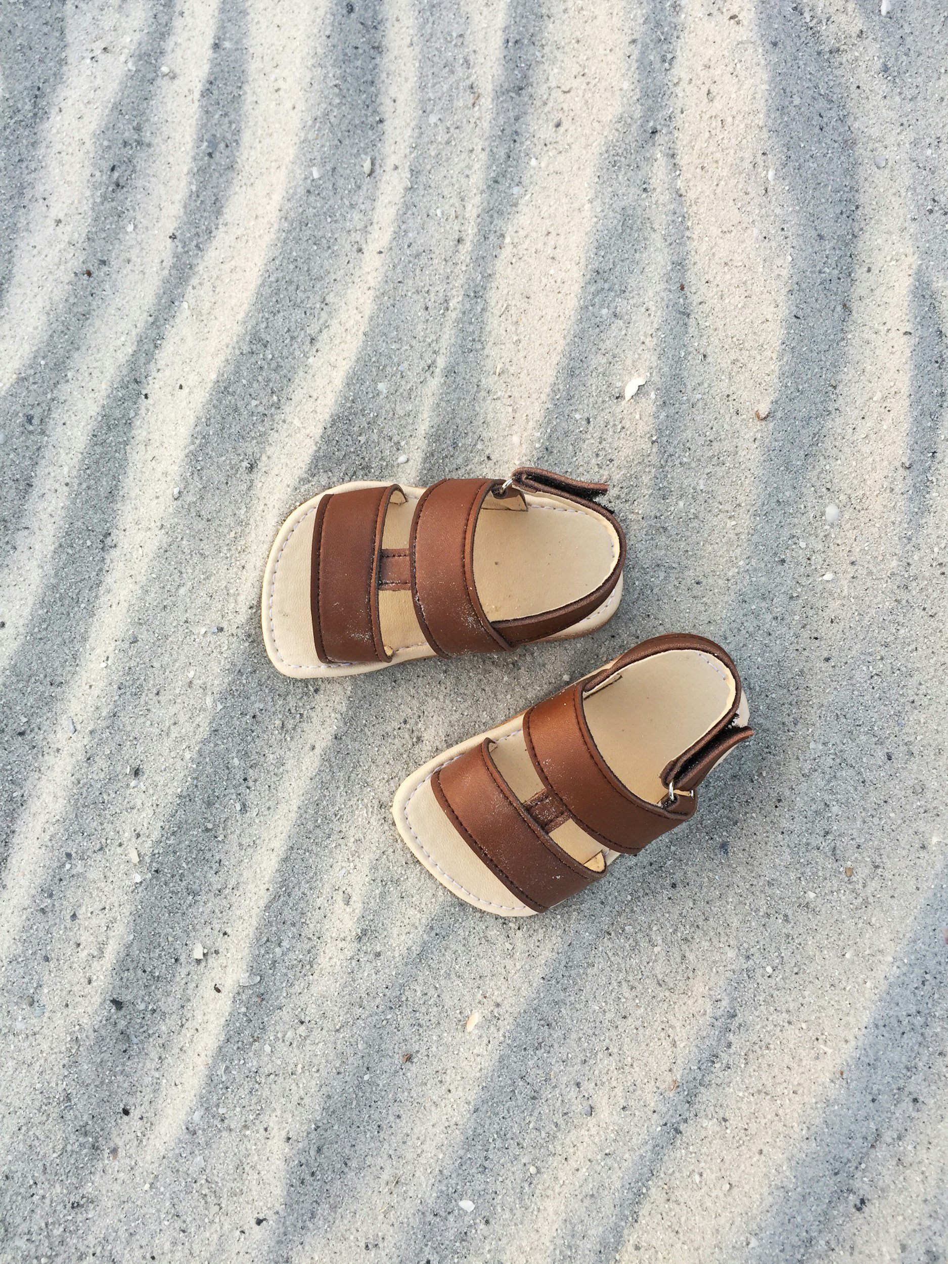 A pair of brown and beige sandals on sandy ground with ripple patterns.
