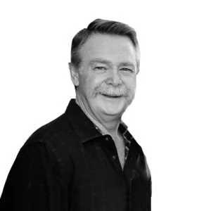 A black and white portrait of an older man with a mustache, smiling and looking at the camera.