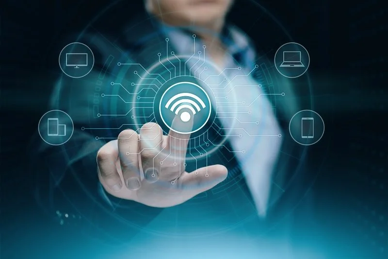 Person touches a digital interface with a Wi-Fi symbol, surrounded by icons of a computer, laptop, tablet, and smartphone, representing technology connectivity.