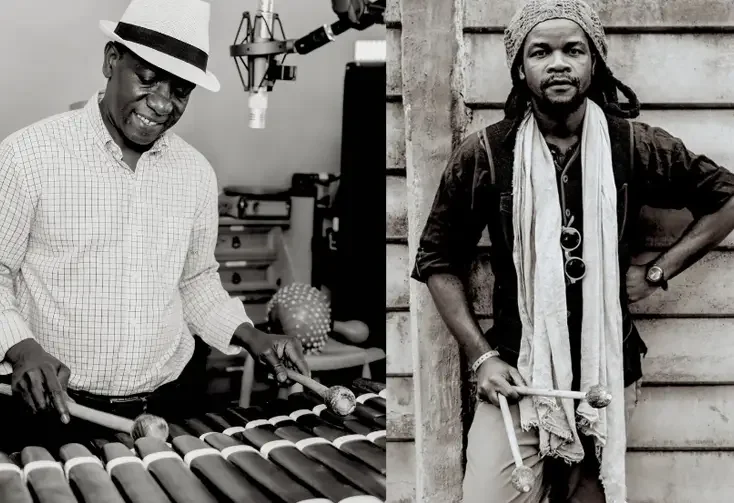 Black and white photo of two men, one playing a xylophone and the other standing outdoors with a drumstick in each hand.