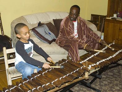 A young girl and an adult man sit on a couch playing a marimba.