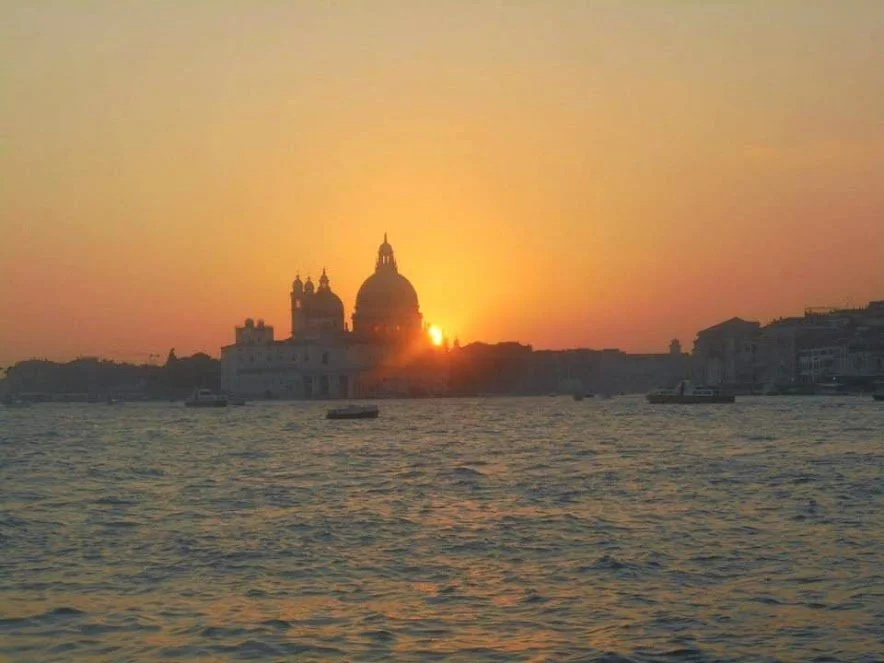 A Photograph taken by Marlena Lambe showcasing a Sunset over a Venis, city skyline with a large domed building and water in the foreground.