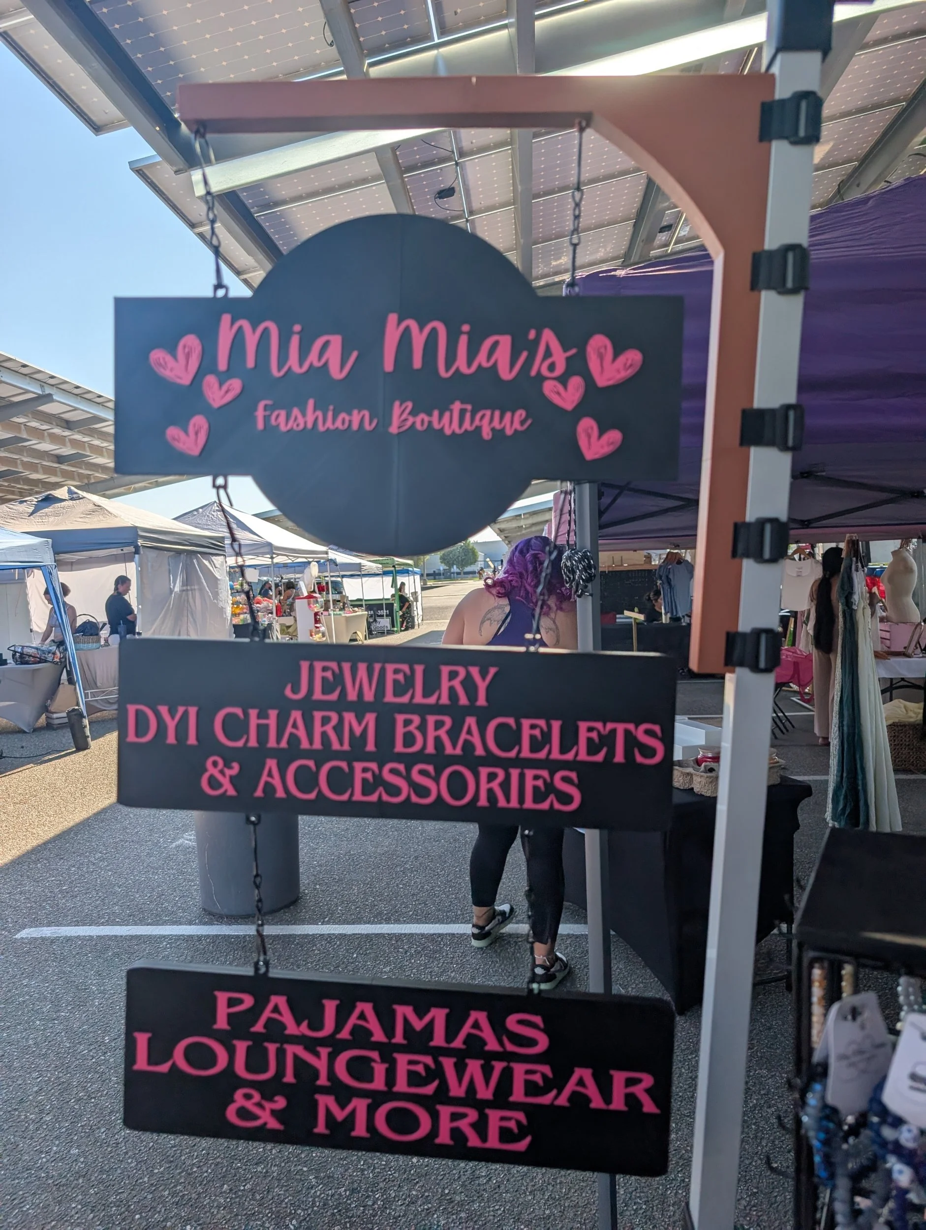 Sign for Mia Mia's Fashion Boutique at an outdoor market, listing jewelry, DIY charm bracelets, accessories, pajamas, loungewear, and more.