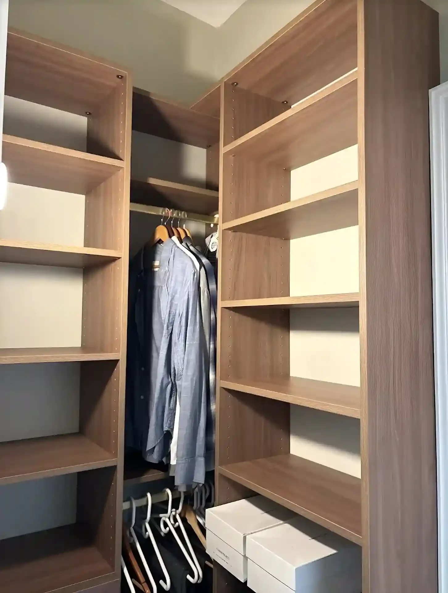 Empty walk-in closet with wooden shelves, clothing on hangers, and storage boxes.