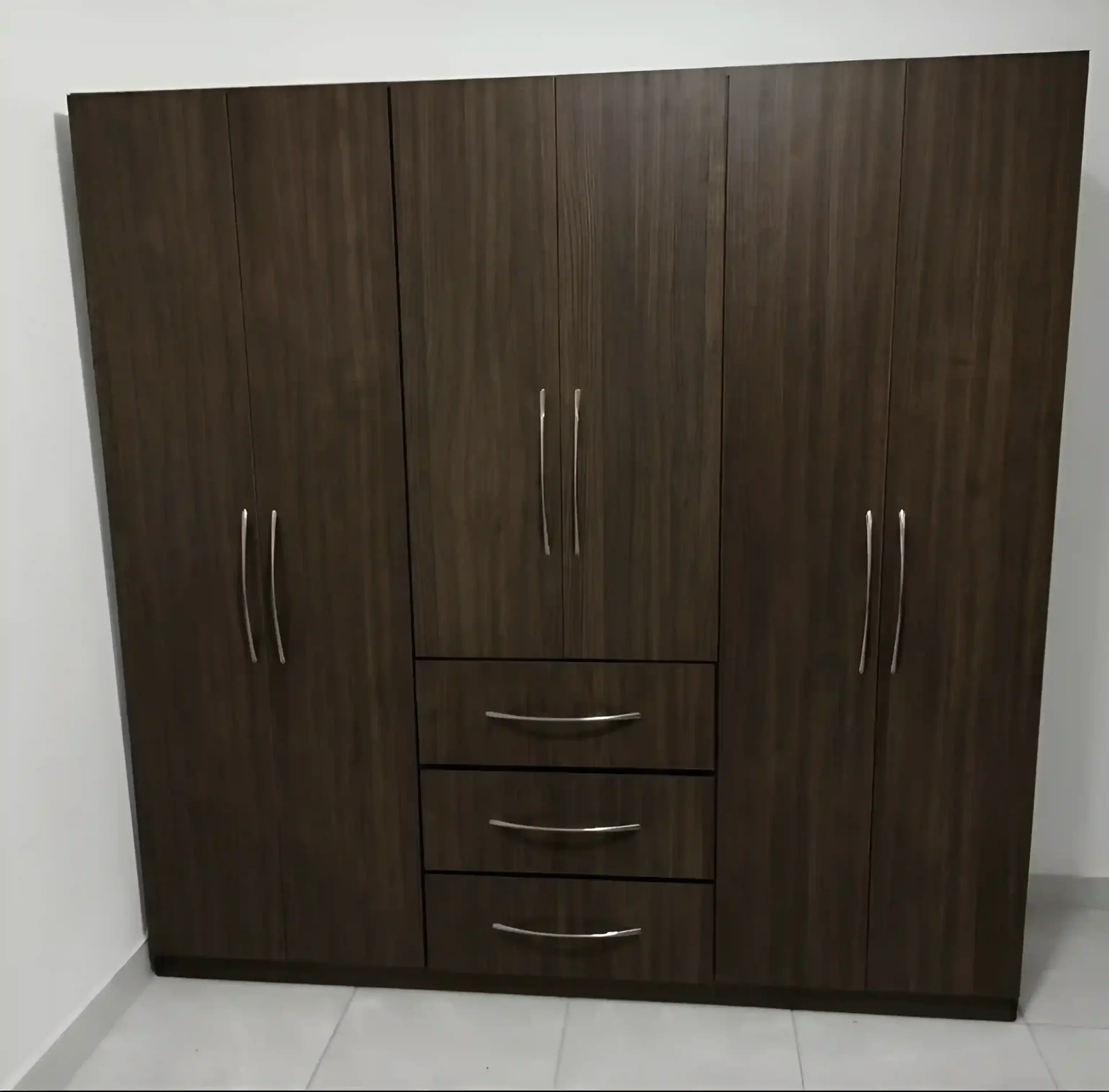 A dark wooden wardrobe with silver handles against a white wall and floor.