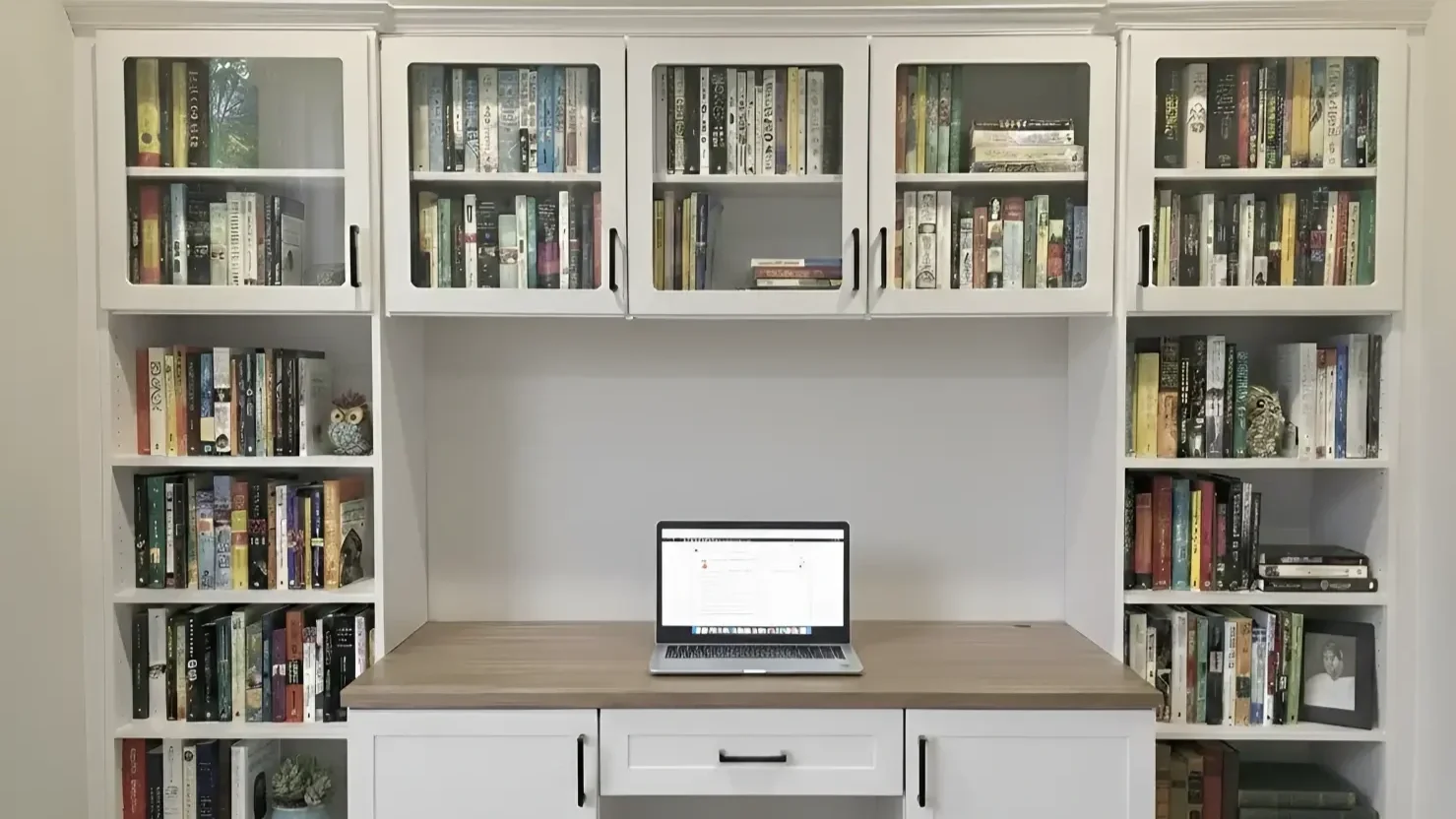 A white home office desk with a laptop, flanked by shelves filled with books and decorative owl figurines.