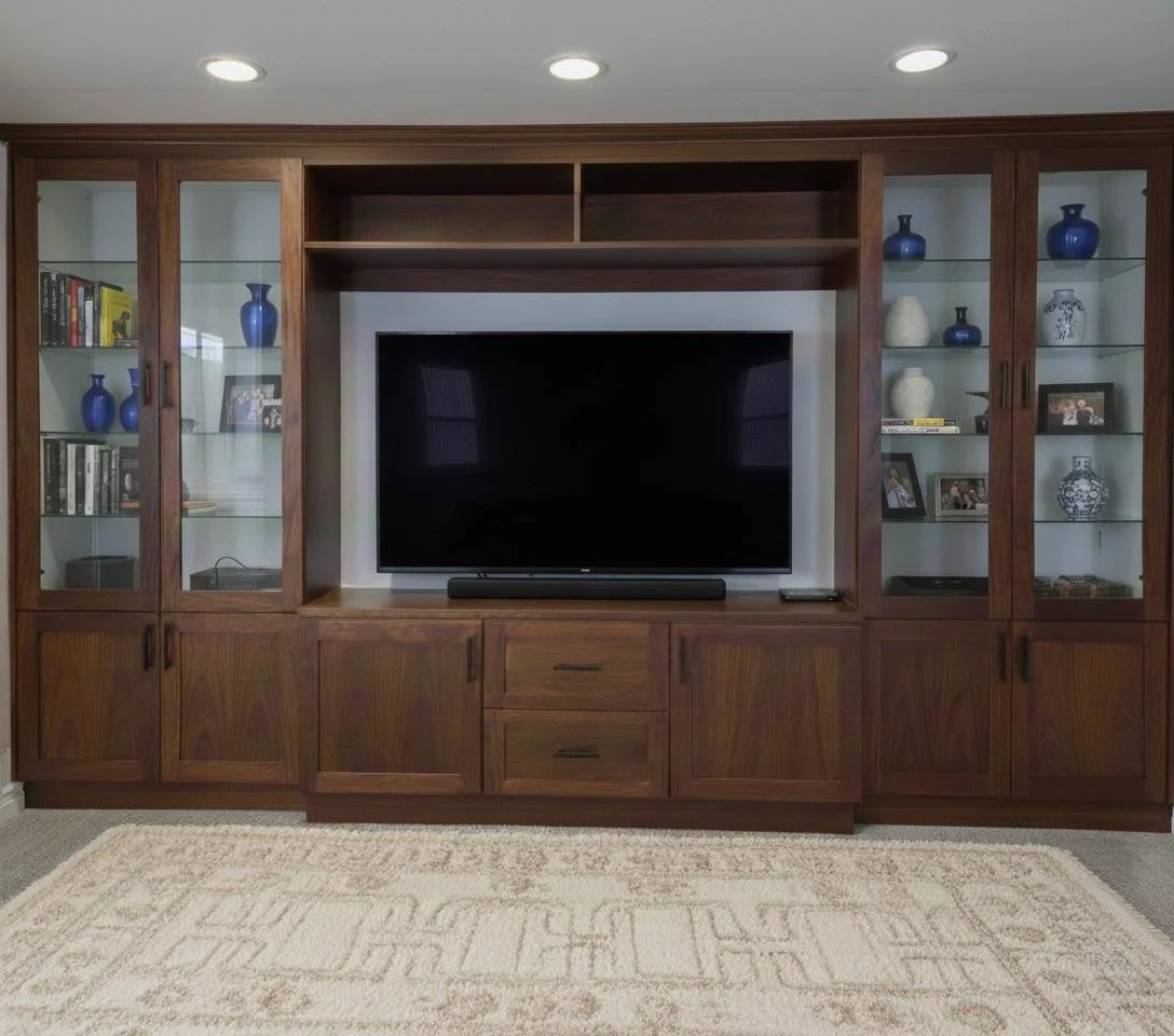 A large wooden entertainment center with glass doors, containing books, decorative vases, and framed photos, surrounds a flat-screen TV in a living room.