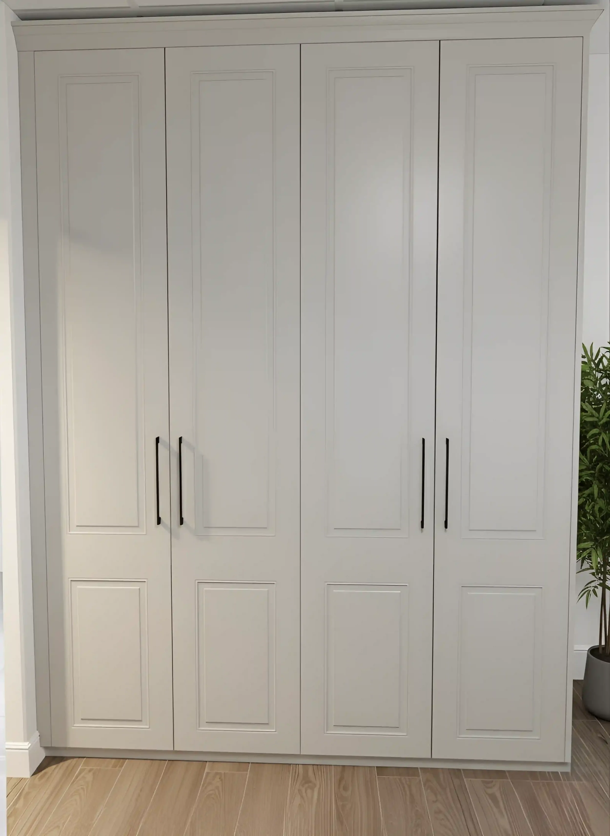 White wardrobe with four paneled doors and black handles, situated in a room with light wood flooring and a potted plant to the side.