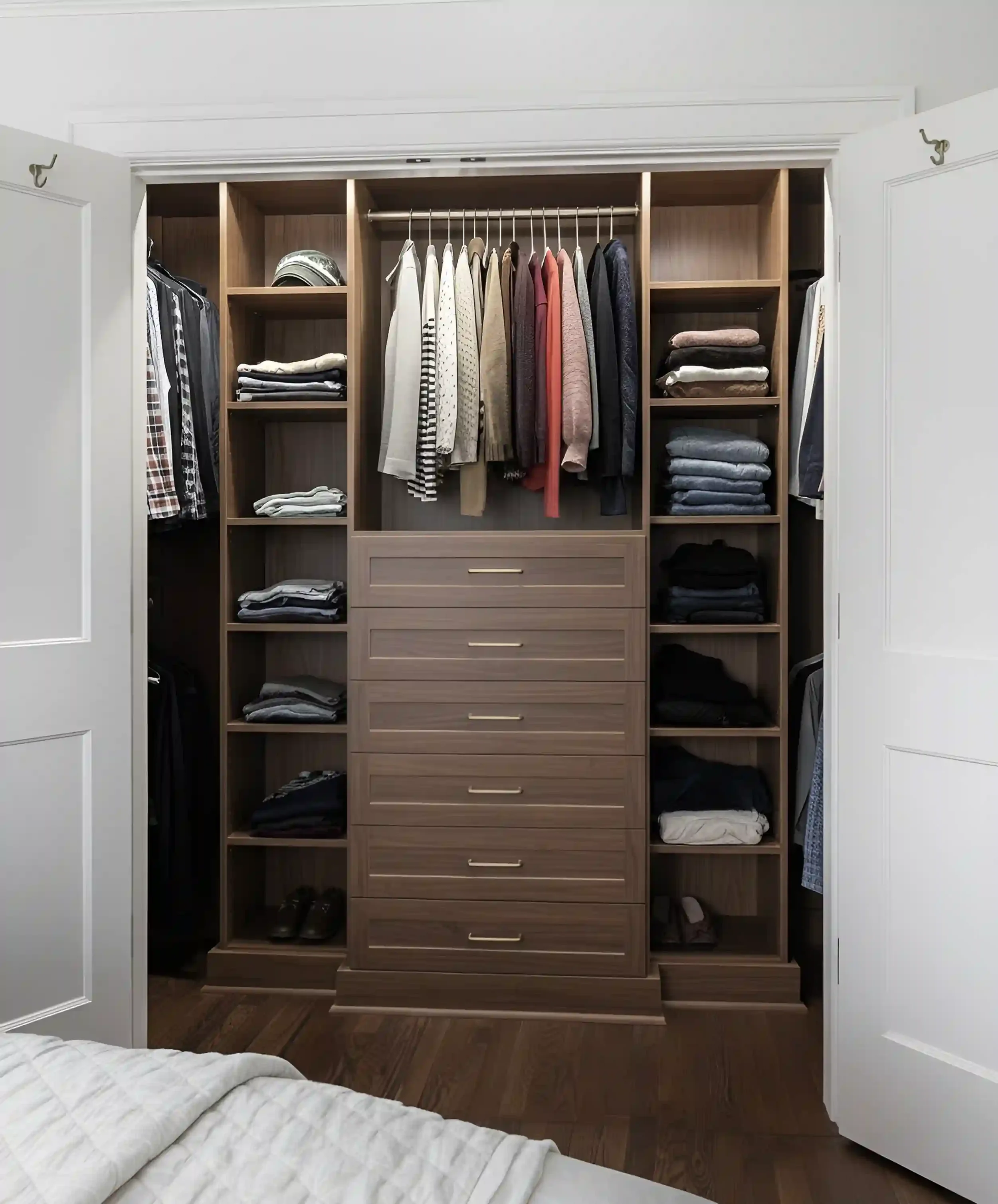 Open closet with hanging clothes, folded clothing on shelves, and drawers, in a bedroom with hardwood flooring.
