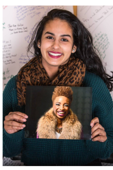 Smiling woman holding a framed photo of another smiling woman with short curly hair and a fur coat.