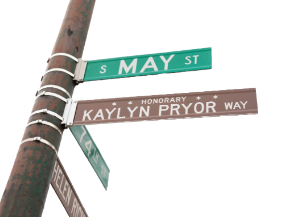 Street signs at an intersection showing 'S May St,' 'Kaylyn Pryor Way,' and 'Helfen Rd' on a rusty utility pole.