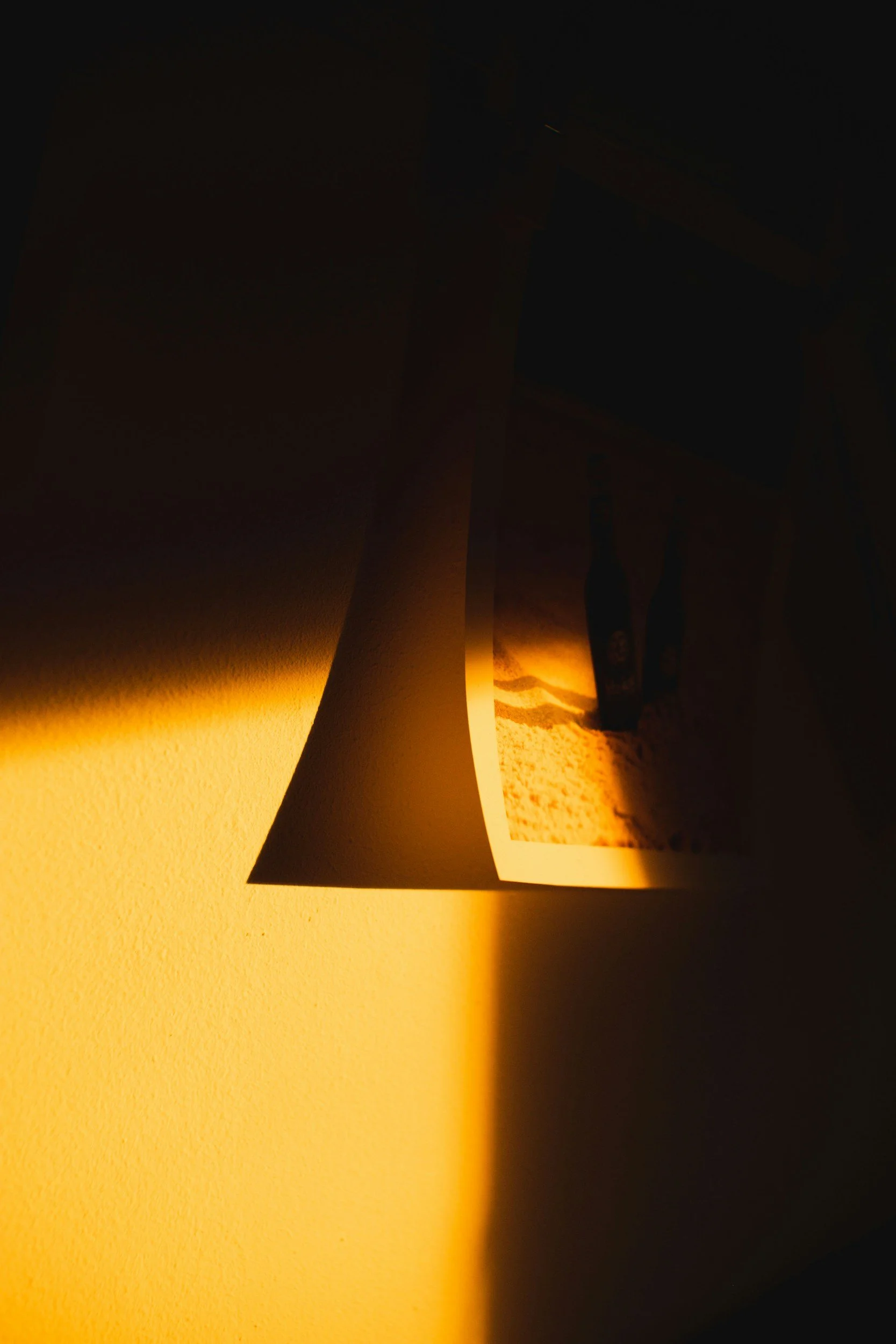 A photograph of a wall with sunlight casting a shadow of a hanging photograph, creating a warm, artistic lighting effect.