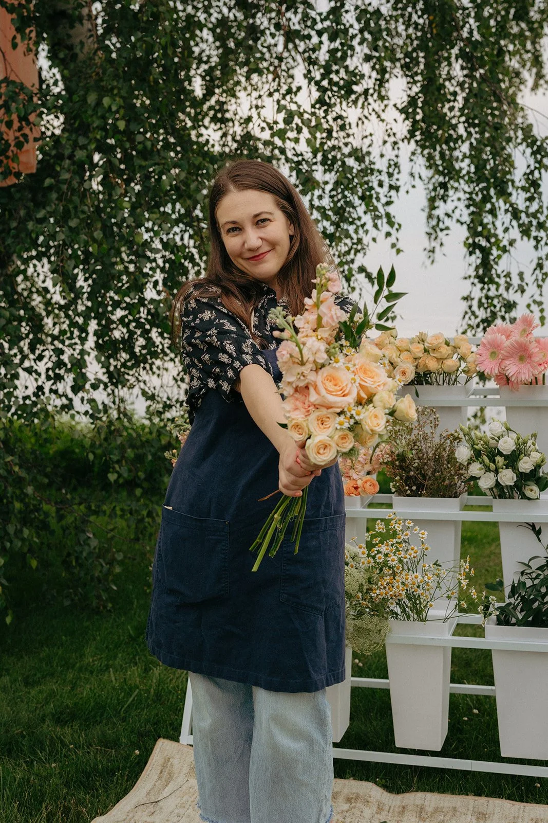 Founder of Little Blue Thistle holding a hand-tied bouquet in front of the Little Blue Thistle mobile flower cart.