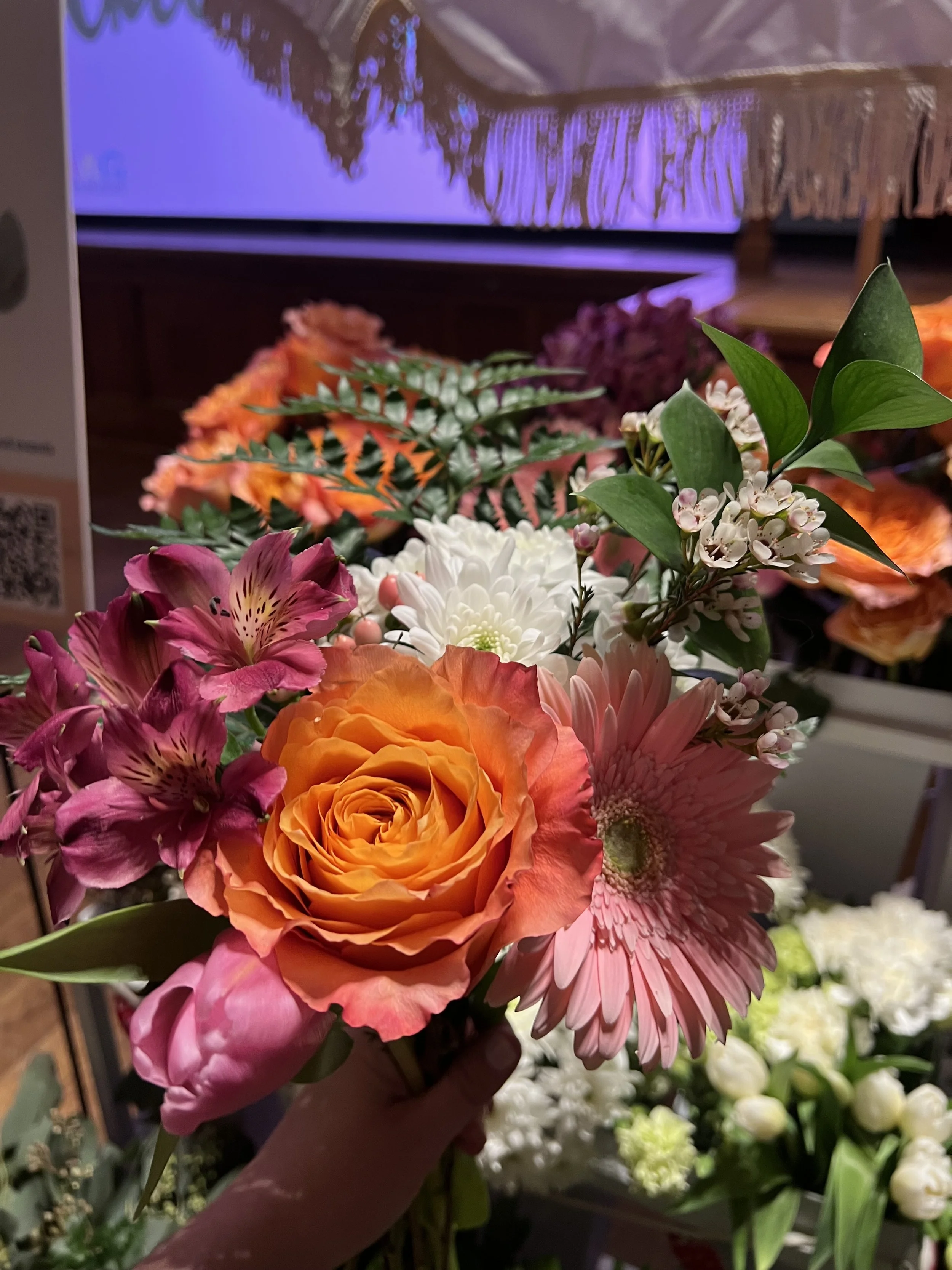 A person holding a bouquet of various colorful flowers including roses, daisies, and other floral arrangements.