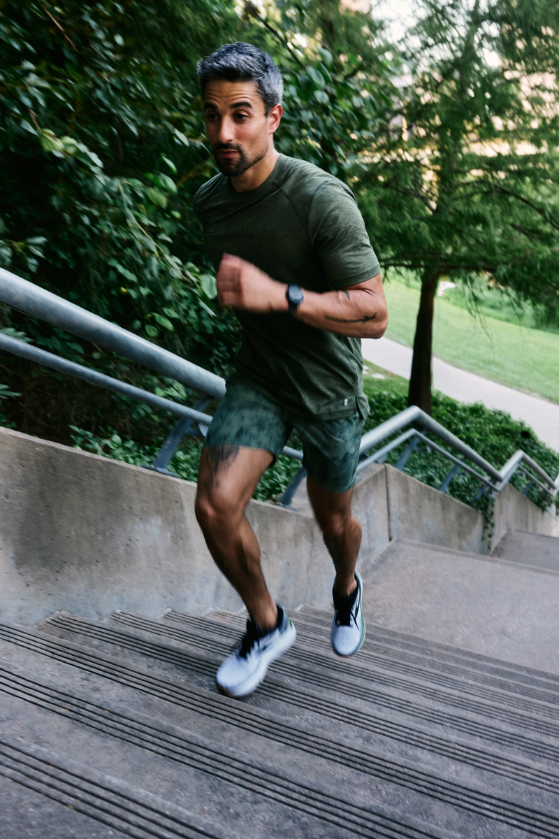 Man running up outdoor concrete stairs with greenery in background.