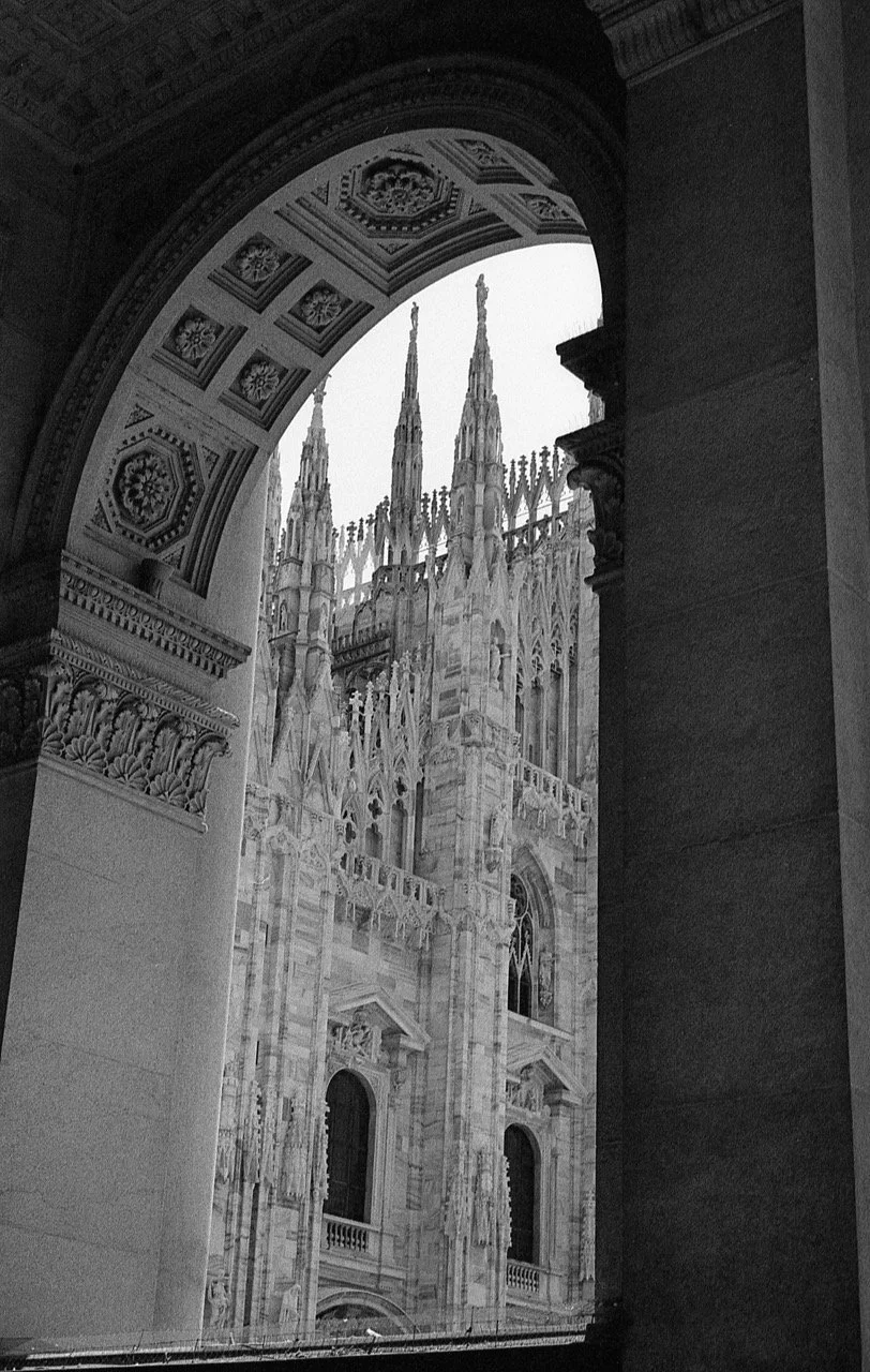 View of the intricate Gothic architecture of Milan Cathedral seen through an archway.