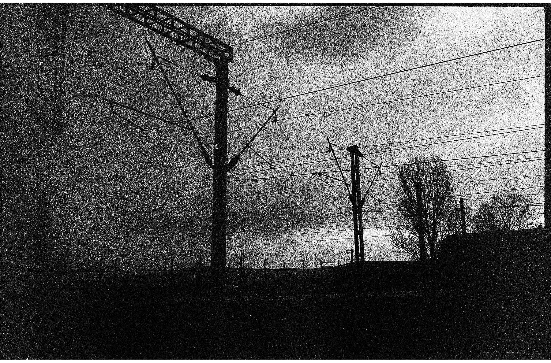 Black and white photo of power lines and utility poles on a hill, with trees and dark clouds in the background.