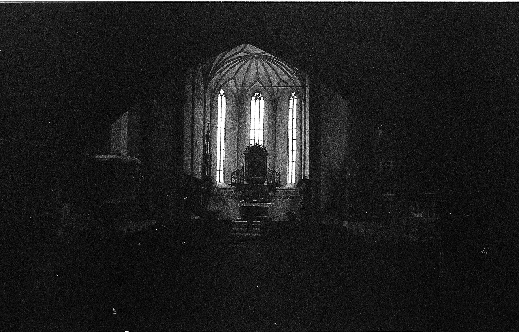 Inside view of a church sanctuary with tall, illuminated stained glass windows and an elevated altar area.