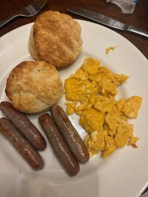 Biscuits, scrambled eggs, and sausage on a white plate.