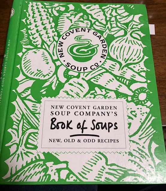 A cookbook with a green cover with an assortment of soup vegetables silhouetted in white.
