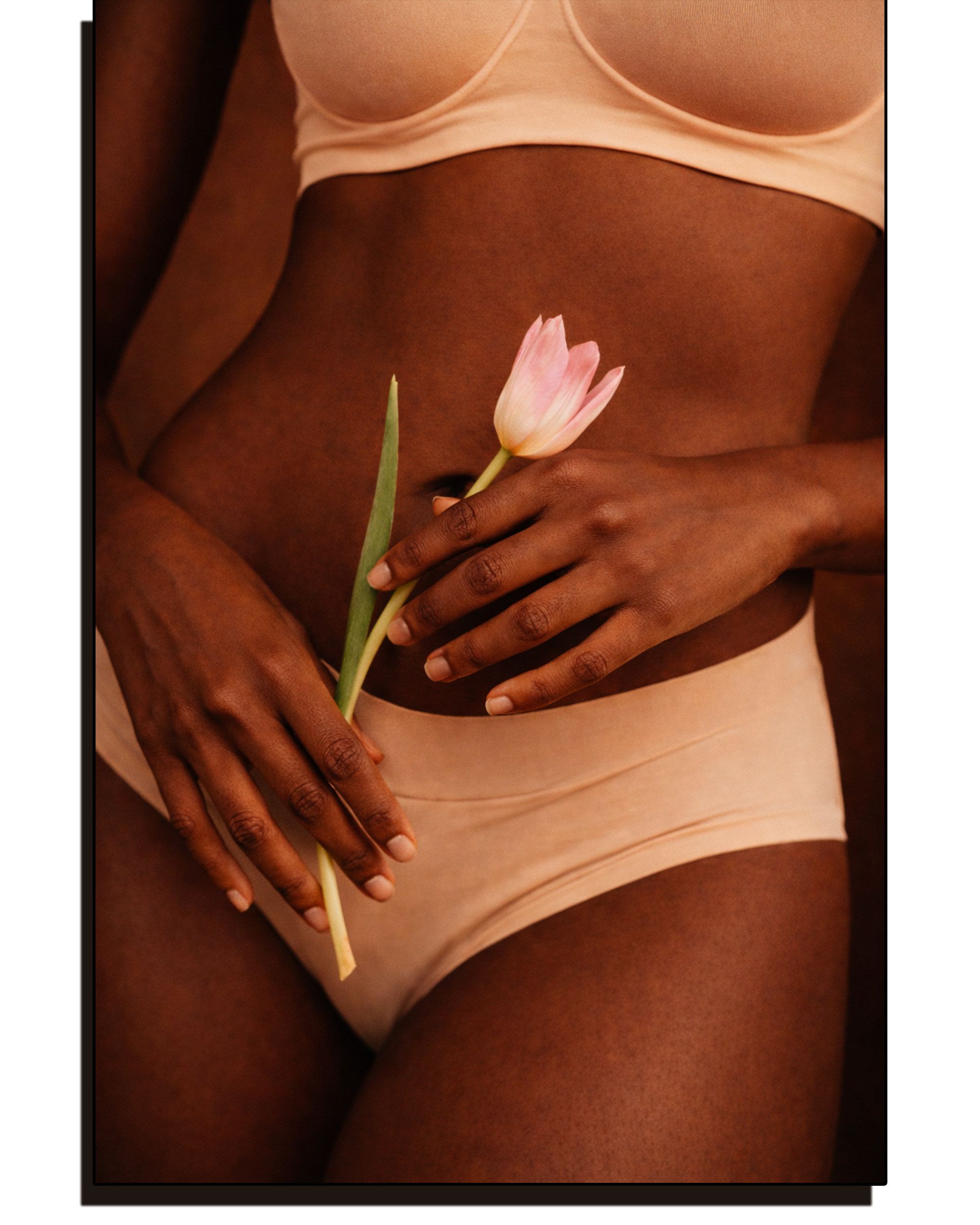 A woman in beige lingerie holding a pink tulip against her lower abdomen.