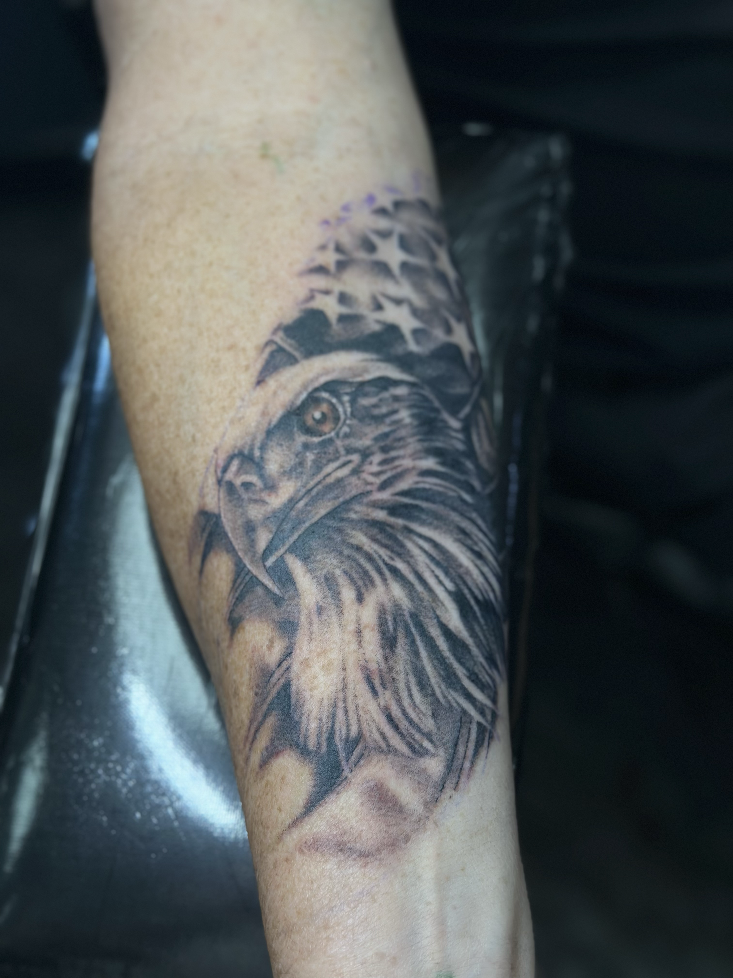 Tattoo of an eagle wearing an American flag bandana on a person's arm.