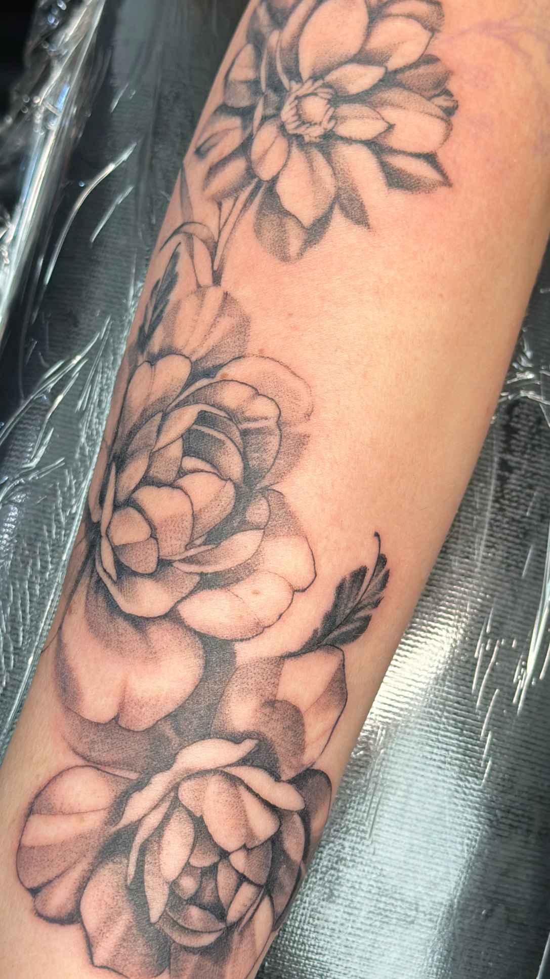 Black and gray floral tattoo on arm depicting peonies with detailed shading and leaves.